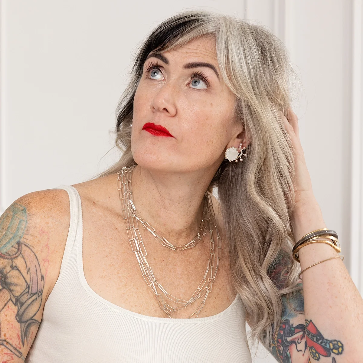 woman with blond hair and tattoos wearing pink pearl hoops and mother of pearl post earrings with white top and red lips