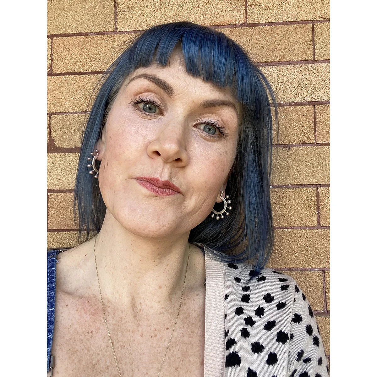 woman with blue hair and leopard cardigan in front of brick wall with pink freshwater pearl hoop earrings
