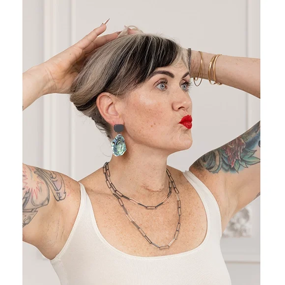 flashy green blue and purple shell earrings with oxidized sterling silver on woman with white tank top red lips and textured backdrop