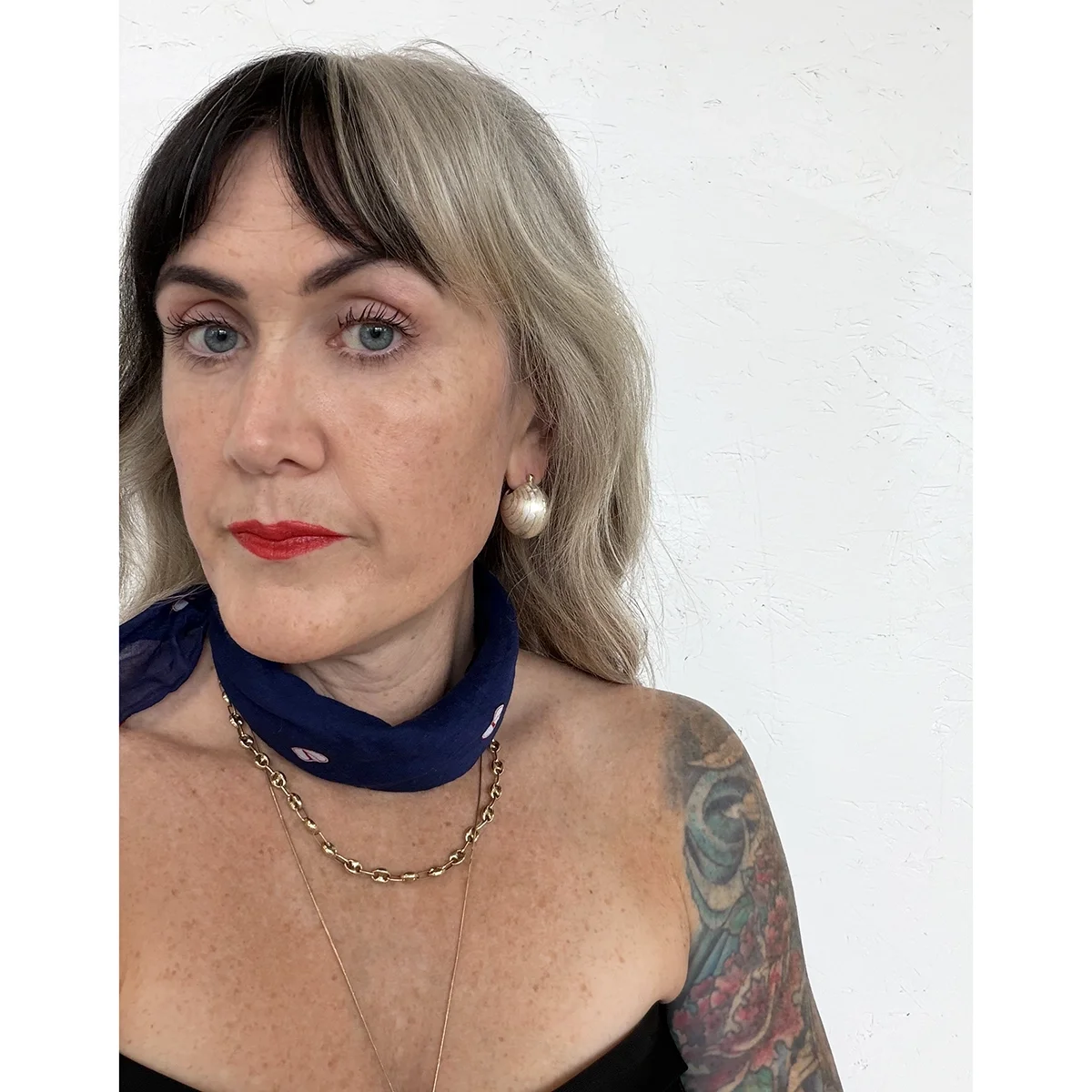 woman with blonde wavy hair, blue eyes, a black strapless top and a blue scarf wearing sterling silver ball earrings with 18k yellow gold lines