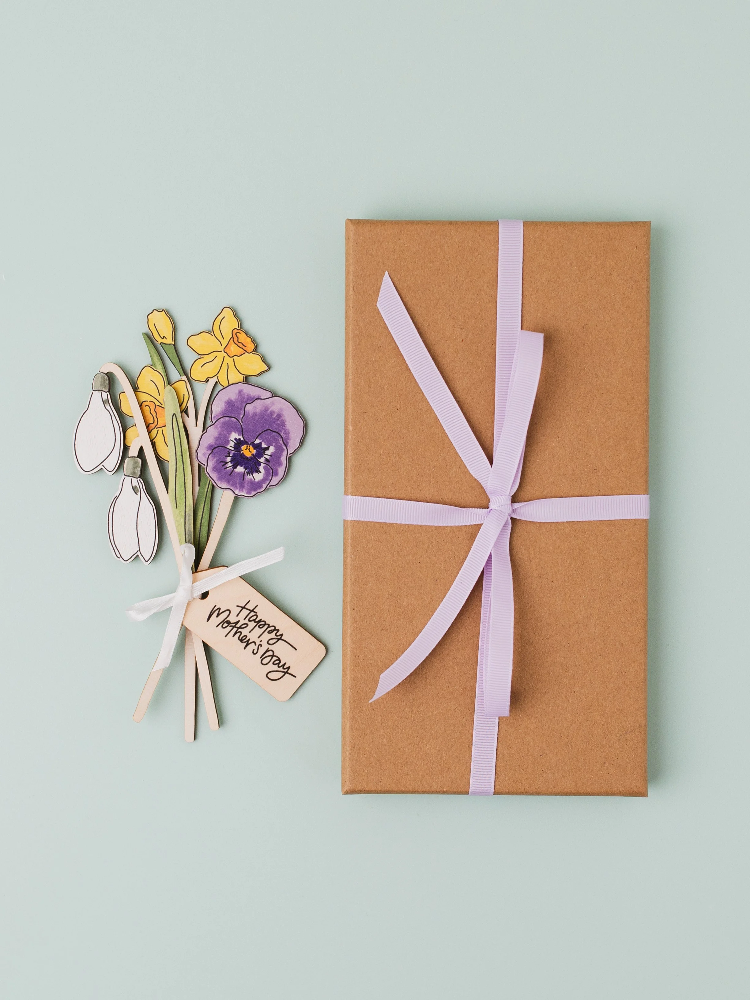Wooden flower bouquet with Mother's Day wooden tag including a violet and daffodils next to gift box wrapped with ribbon