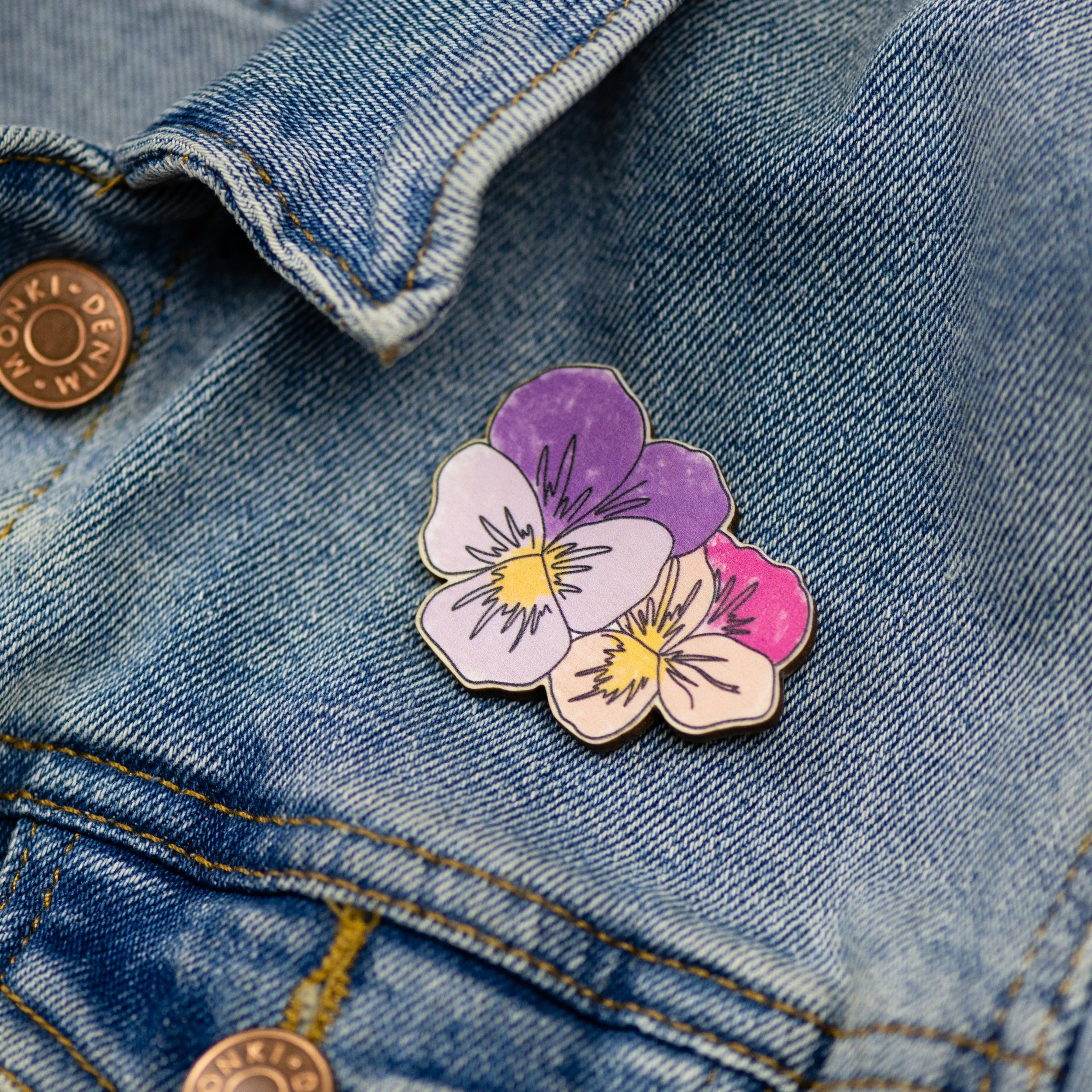 A wooden violet flower brooch depicting two flowers, one purple tones and one in shades of pink