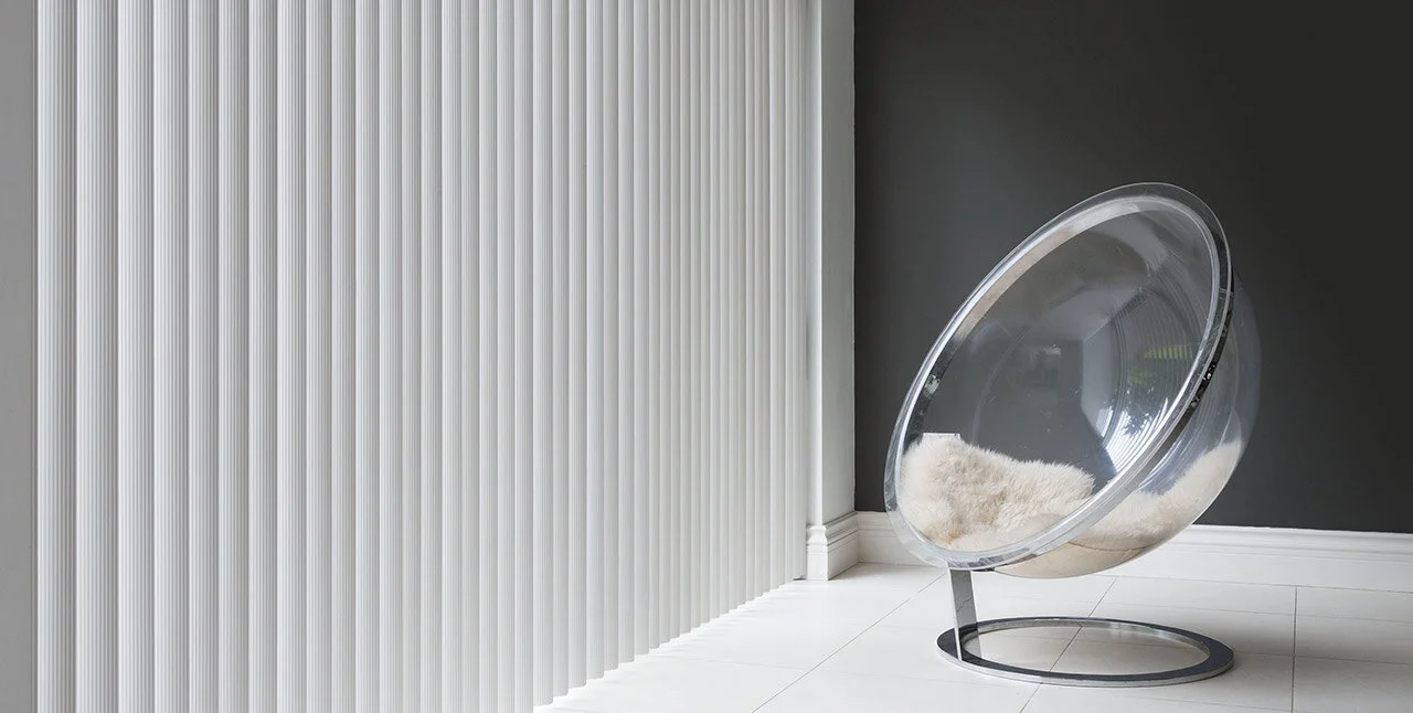Modern transparent egg-shaped chair with white cushion in corner of a room with white and dark gray walls and white tiled floor.