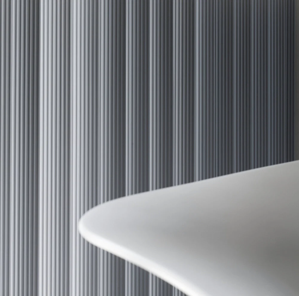 Close-up of a white surface, likely a piece of modern architectural furniture or decor, with a background of vertical metallic strips with a reflective surface.