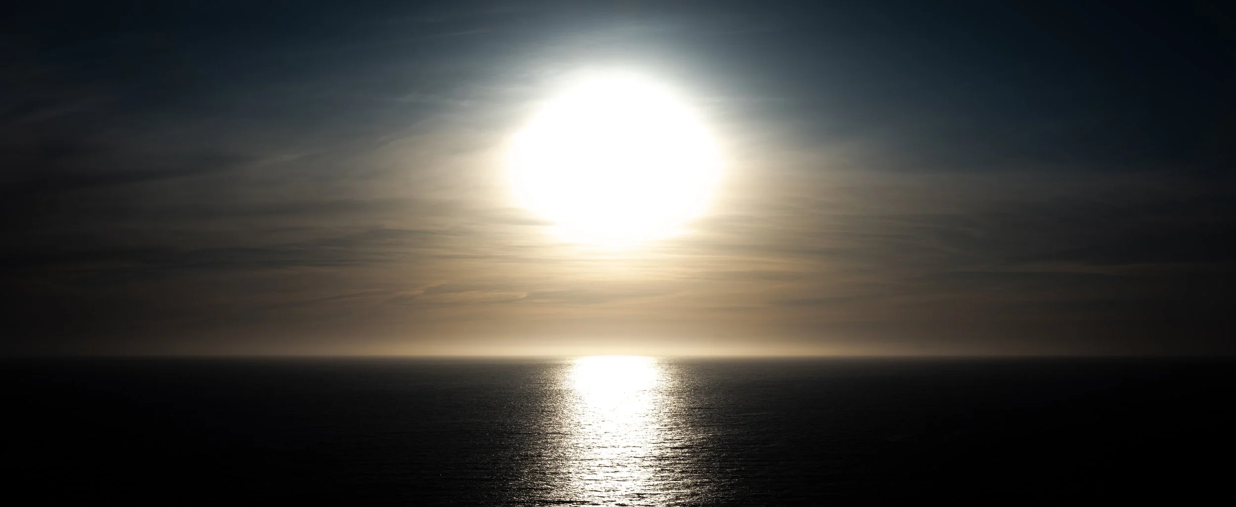 Sunset over the ocean with a reflective water surface and a partly cloudy sky.