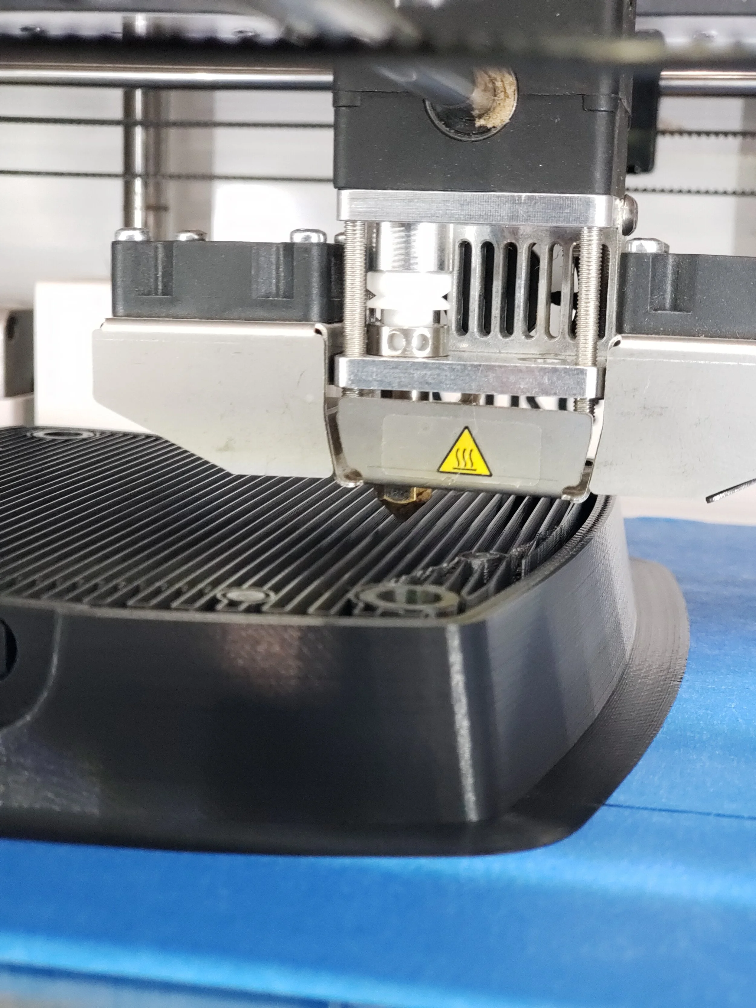 Close-up of a 3D printer nozzle extruding a black plastic object.