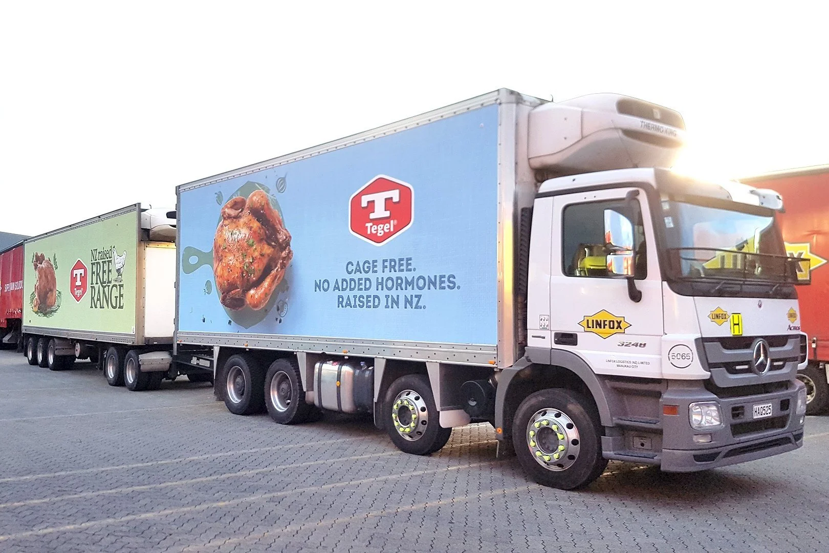 A truck with trailers featuring Tegel branding, showcasing roast chicken images and text promoting 'cage-free' and 'no added hormones' products, parked on a paved surface.