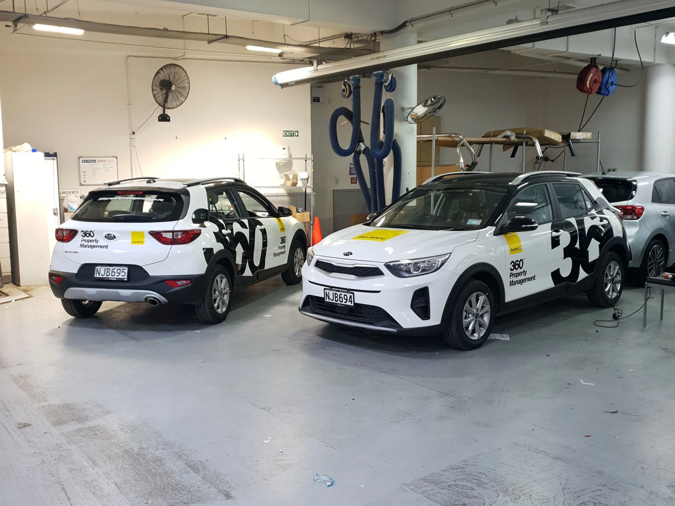 Two white Kia SUVs with "360 Property Management" decals parked in a garage.