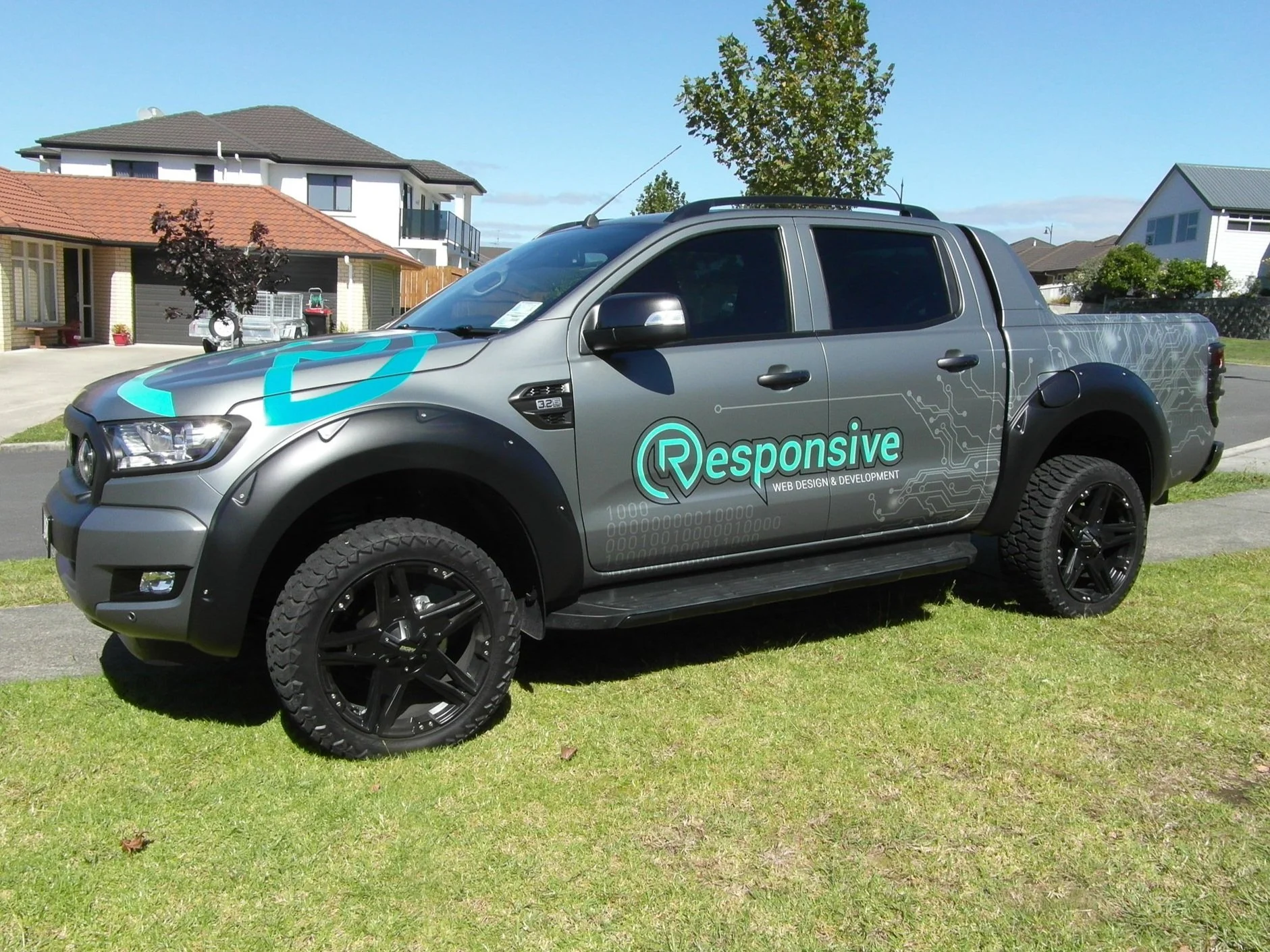 Gray pickup truck with 'Responsive Web Design & Development' branding parked on grass in a suburban neighborhood.