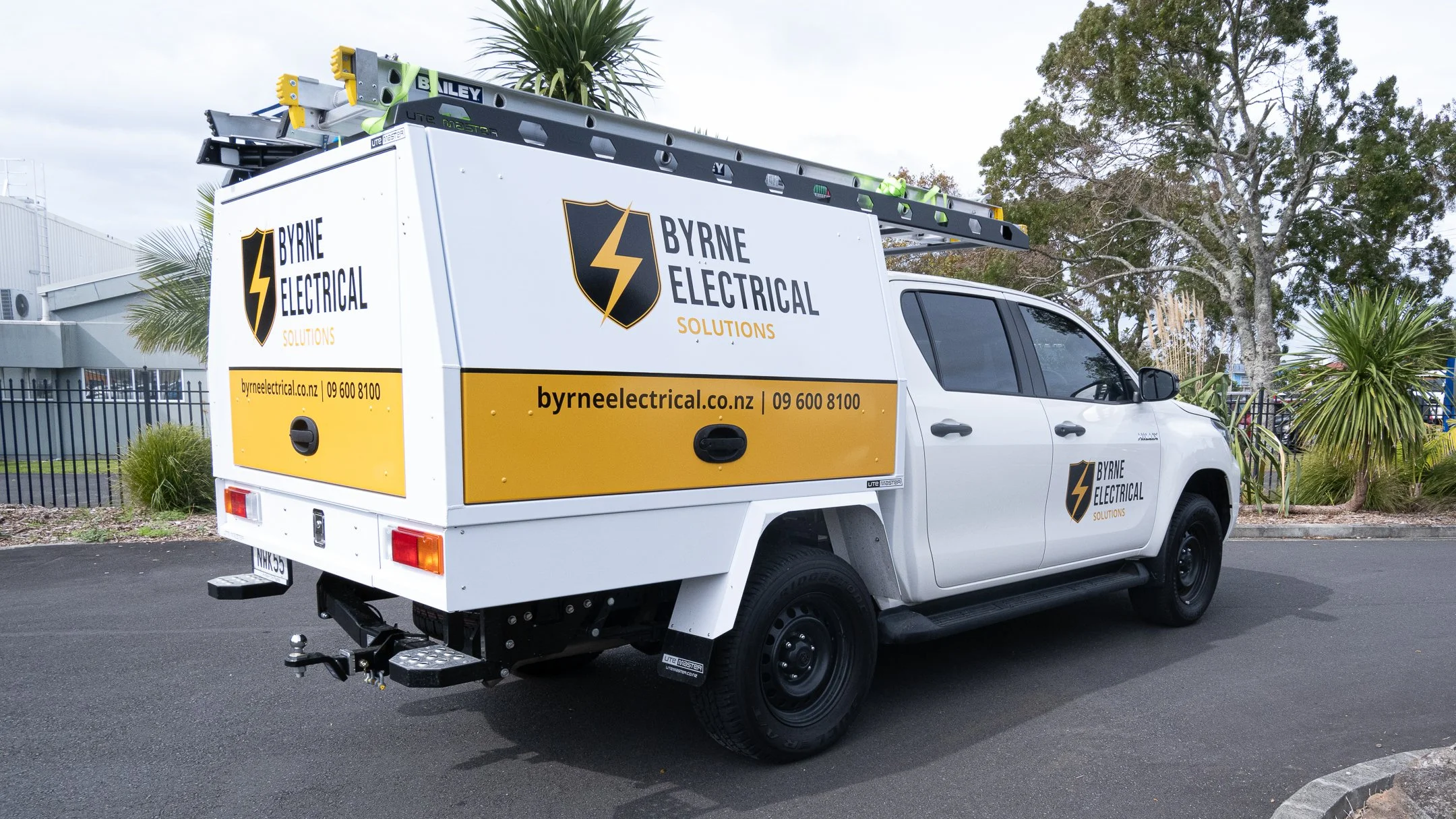 White utility truck with Byrne Electrical Solutions branding, parked on pavement, equipped with ladders and company contact information displayed on the vehicle panels.