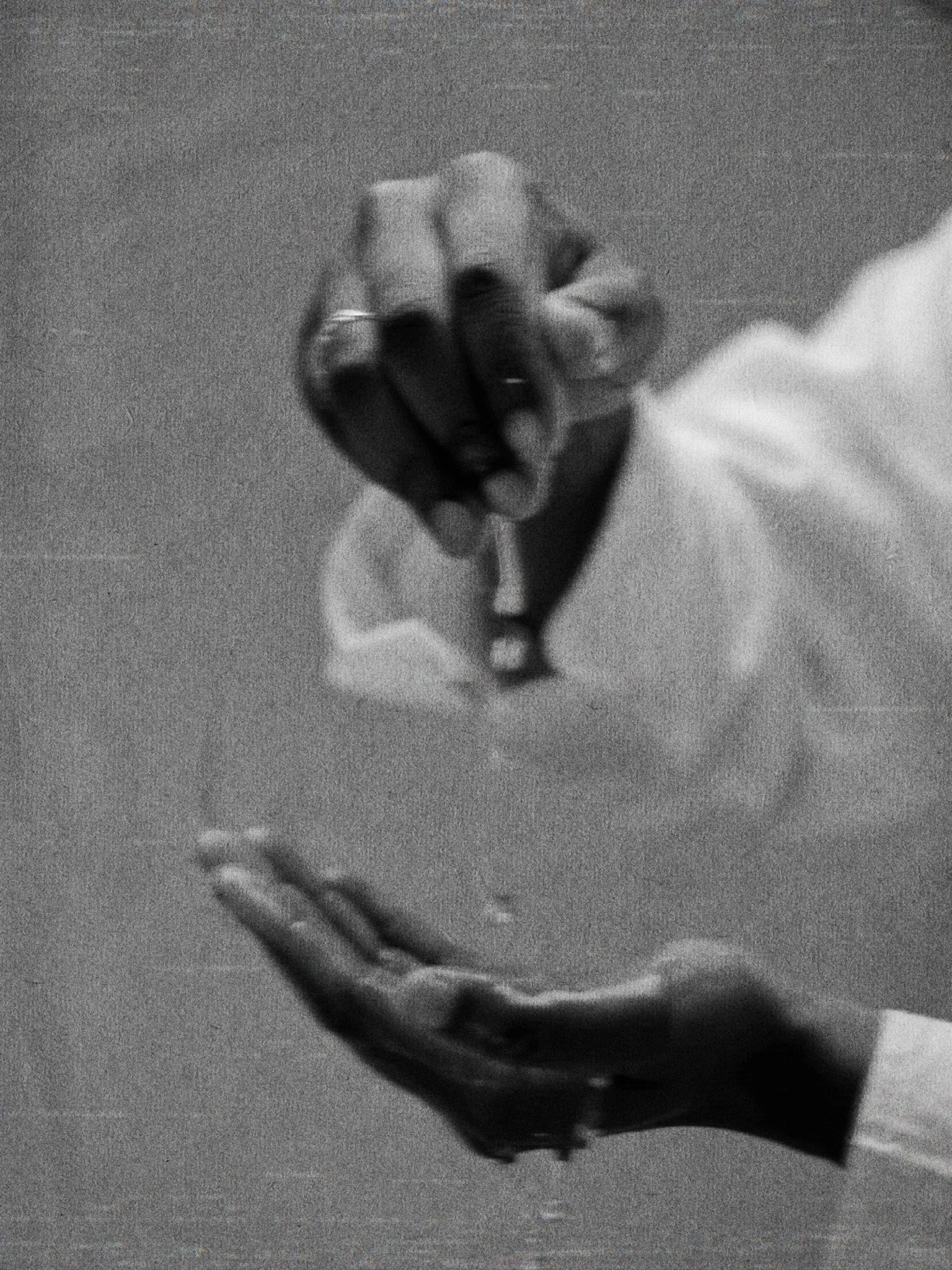 Close-up black and white photo of a person wearing a long sleeve shirt, with one hand raised and clenched in a fist near the camera, and the other hand pointed downward.