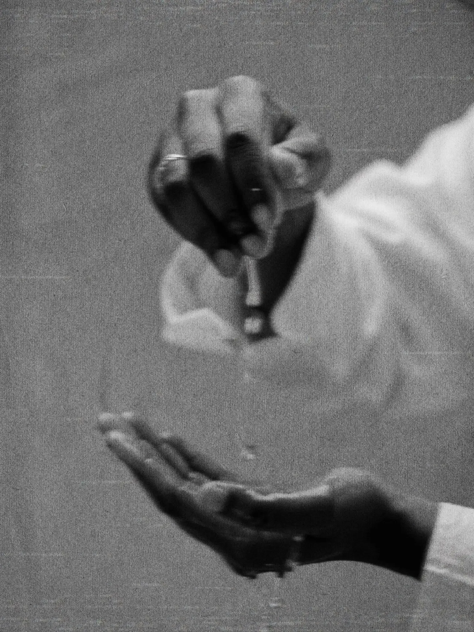 Black and white photograph of two hands clasped together, one hand with rings and a watch, held against a textured background.