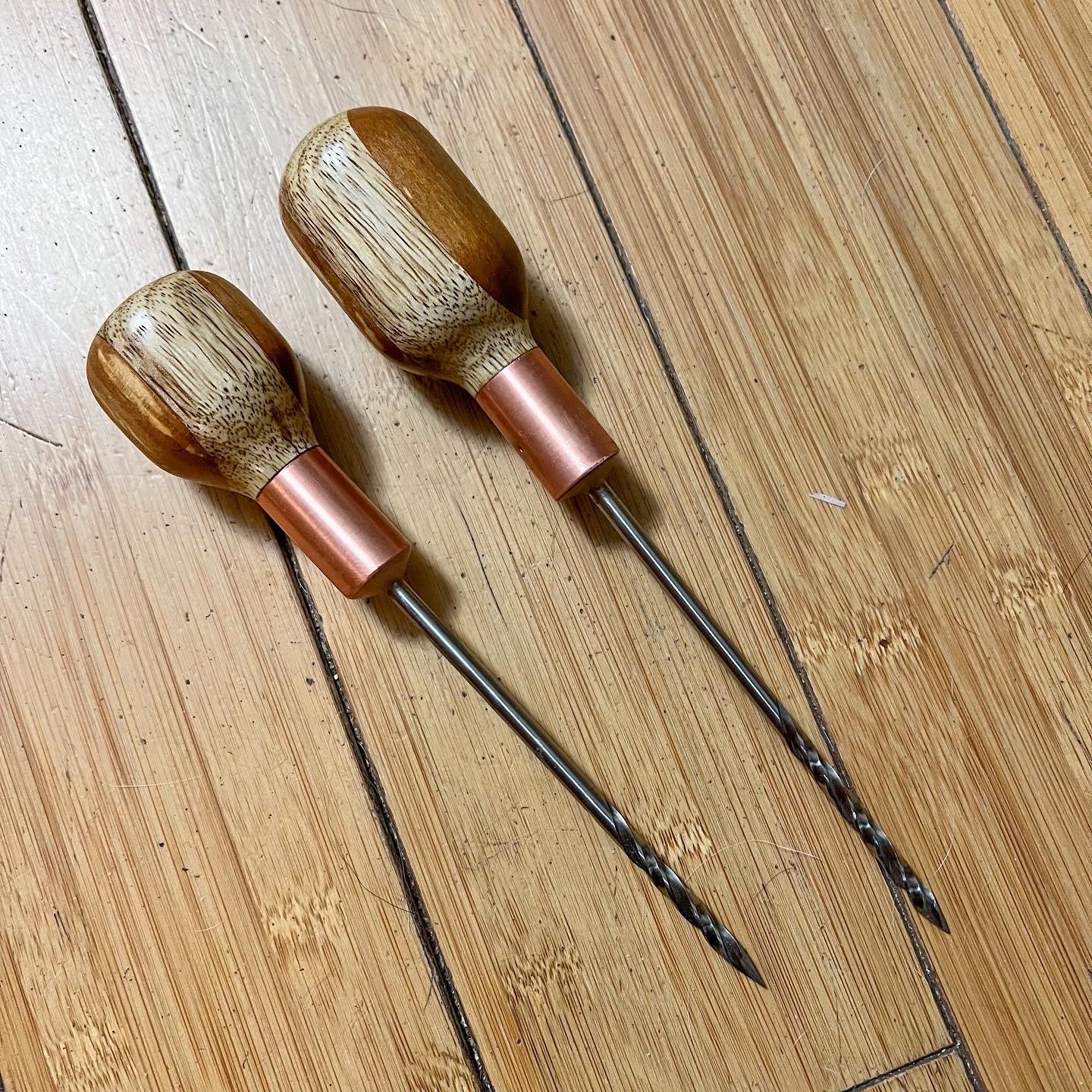 Two wooden-handled awls with metal shafts on a wooden surface.