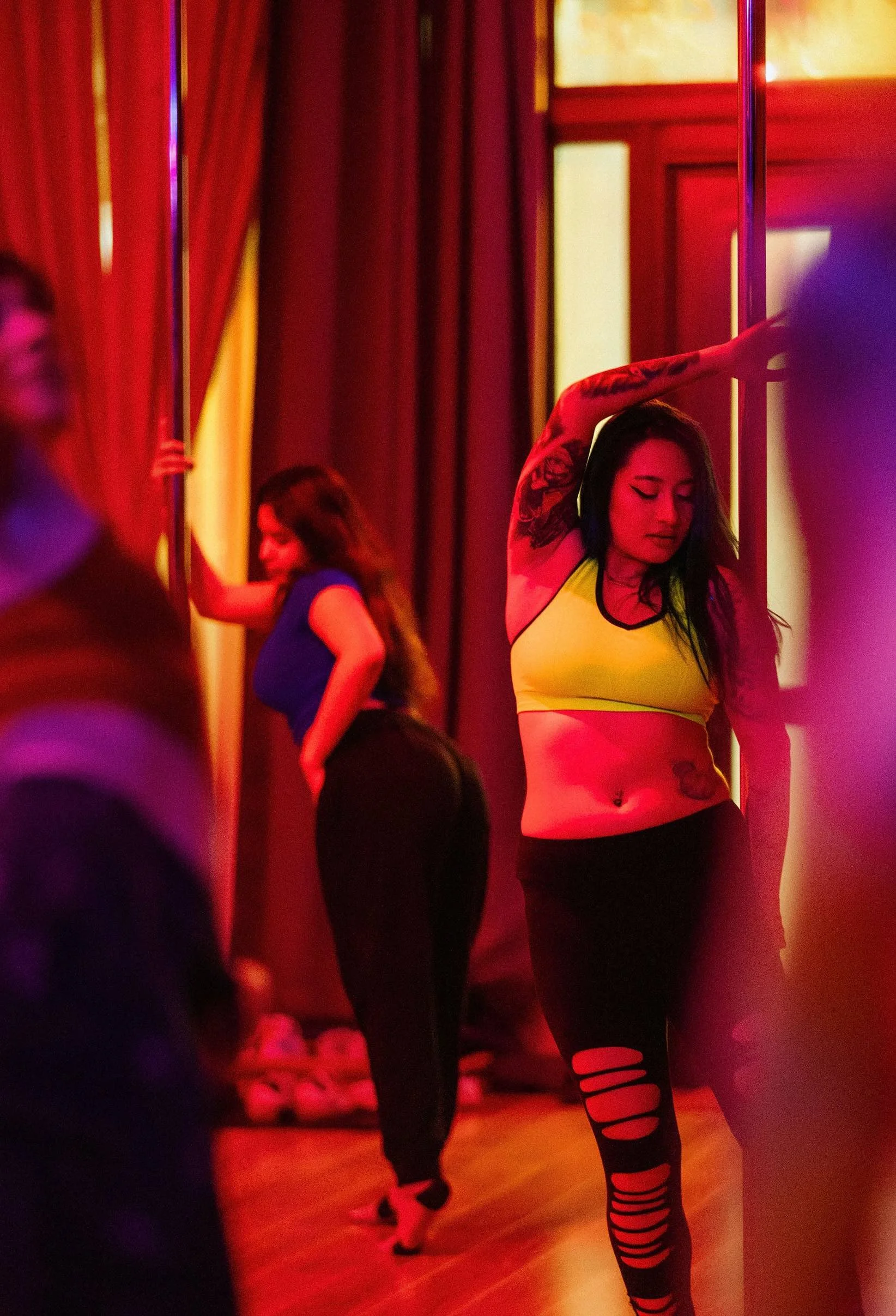 Women pole dancing in a red and purple lit room