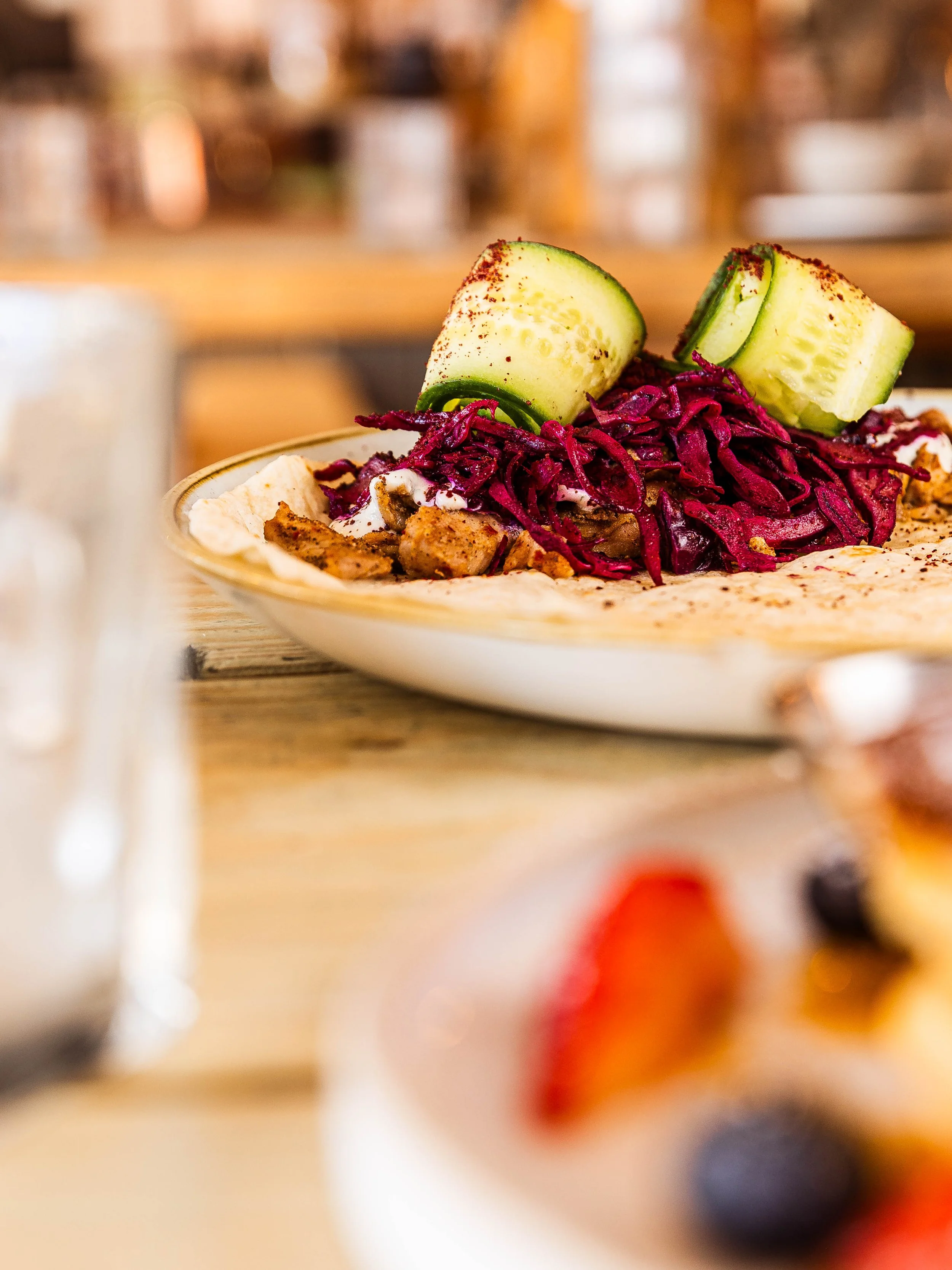 Plate of food with grilled chicken, shredded purple cabbage, cucumber slices, and flatbread on a wooden table. café in Northcote Road, London