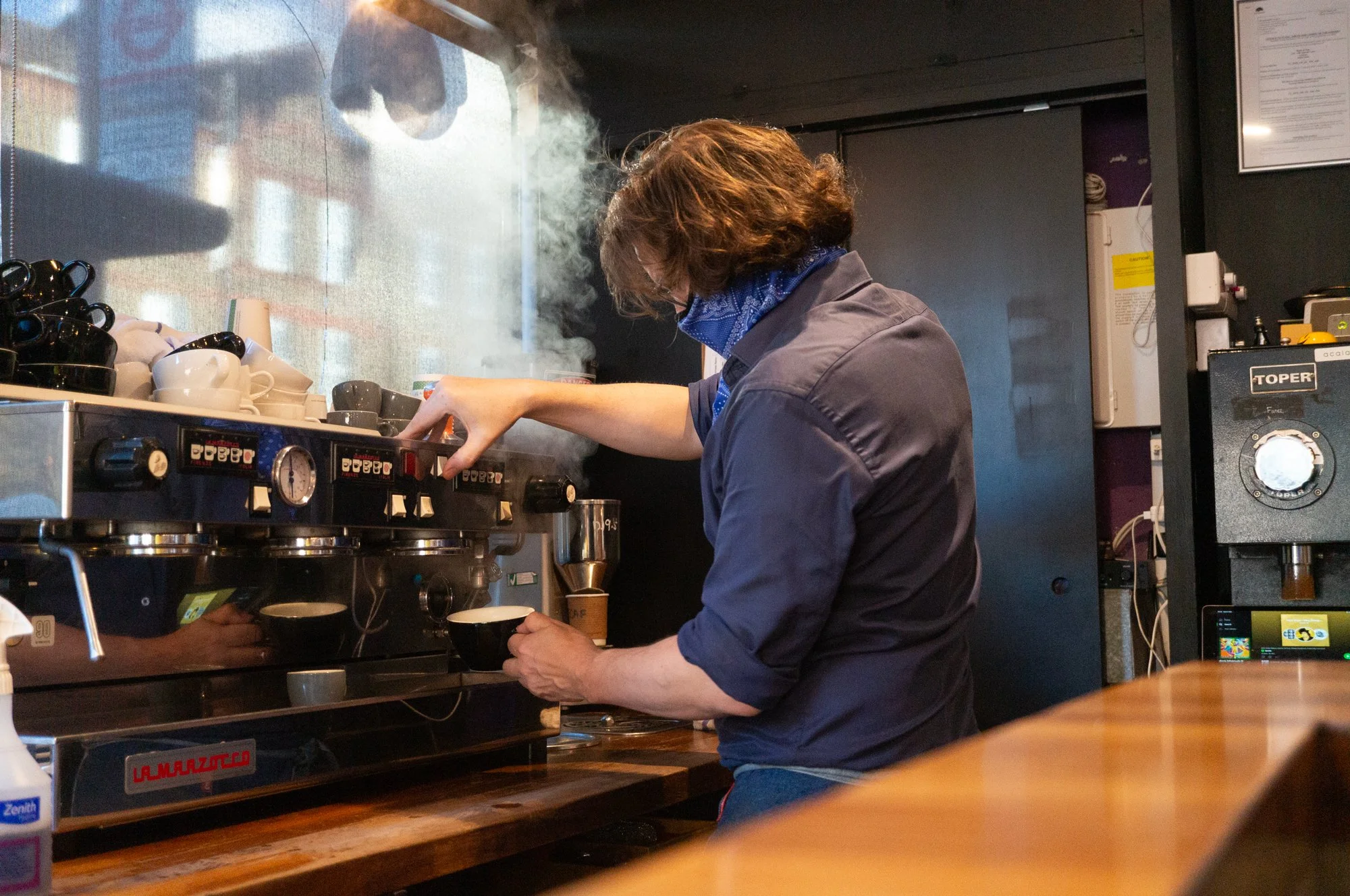 Rob, one of the founders, wearing a blue bandana and grey shirt, making espresso at Cafe Tamra, a barista coffee London