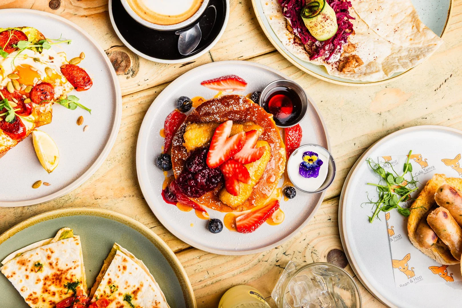Bold flavours and colourful brunch plates. Assorted brunch dishes on a wooden table, including pancakes with strawberries and blueberries, a vegetable pizza, and a wrap with greens. Healthy brunch that’s full of flavour