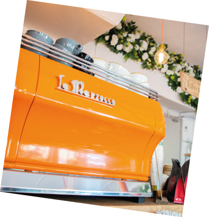 Orange La Marzocco espresso machine with cups on top and a decorated counter in the background. barista coffee London.