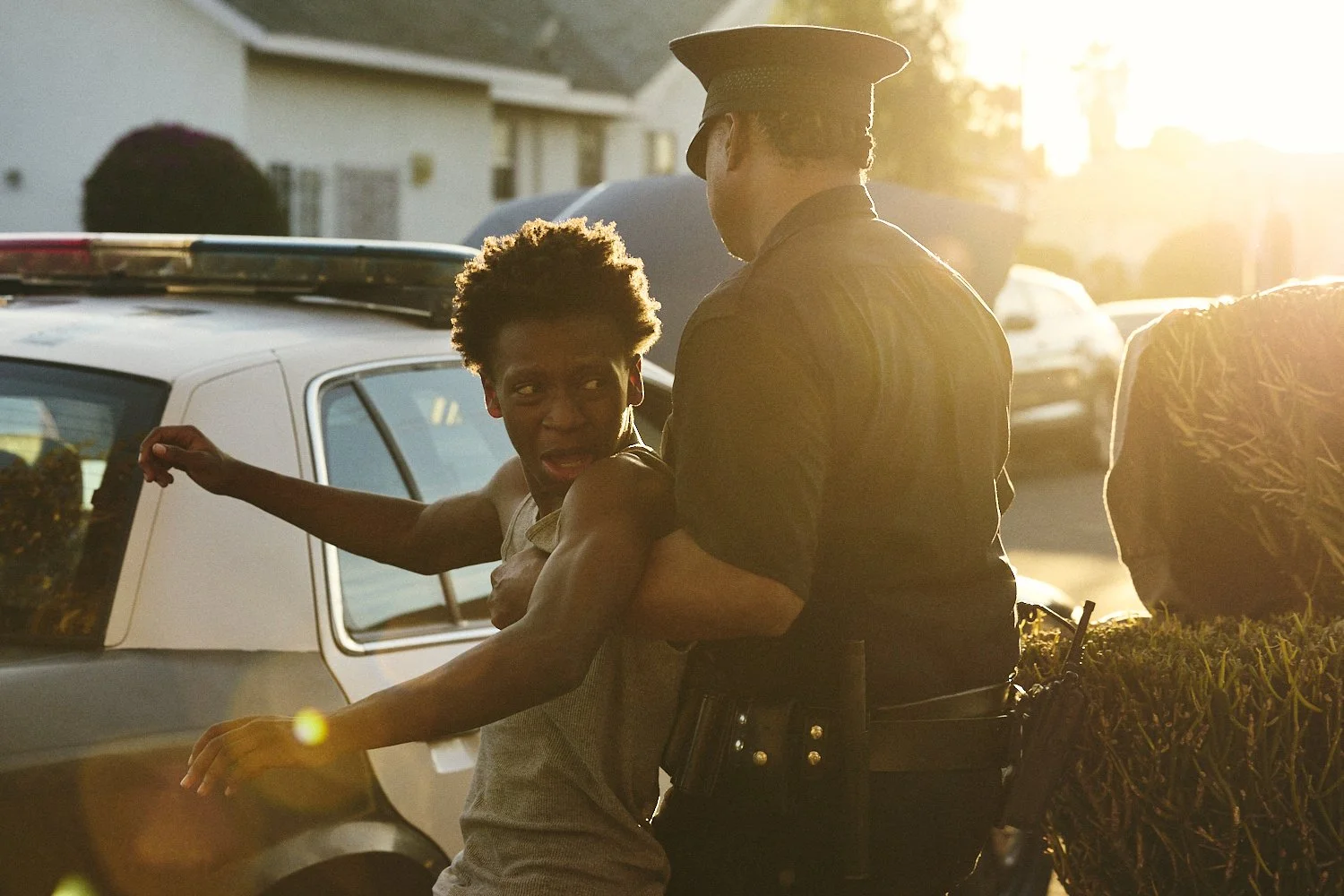 Professional film still of a young black man, with short curly hair, being handcuffed by a police officer, during sunset for the short film "Now You Lay Me."