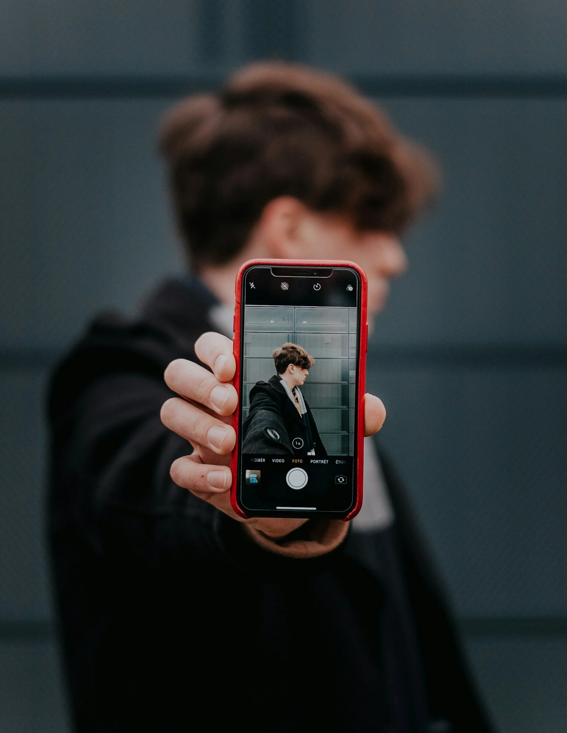 Persoon neemt selfie met smartphone in een donkere ruimte, gezicht en achtergrond zijn wazig.