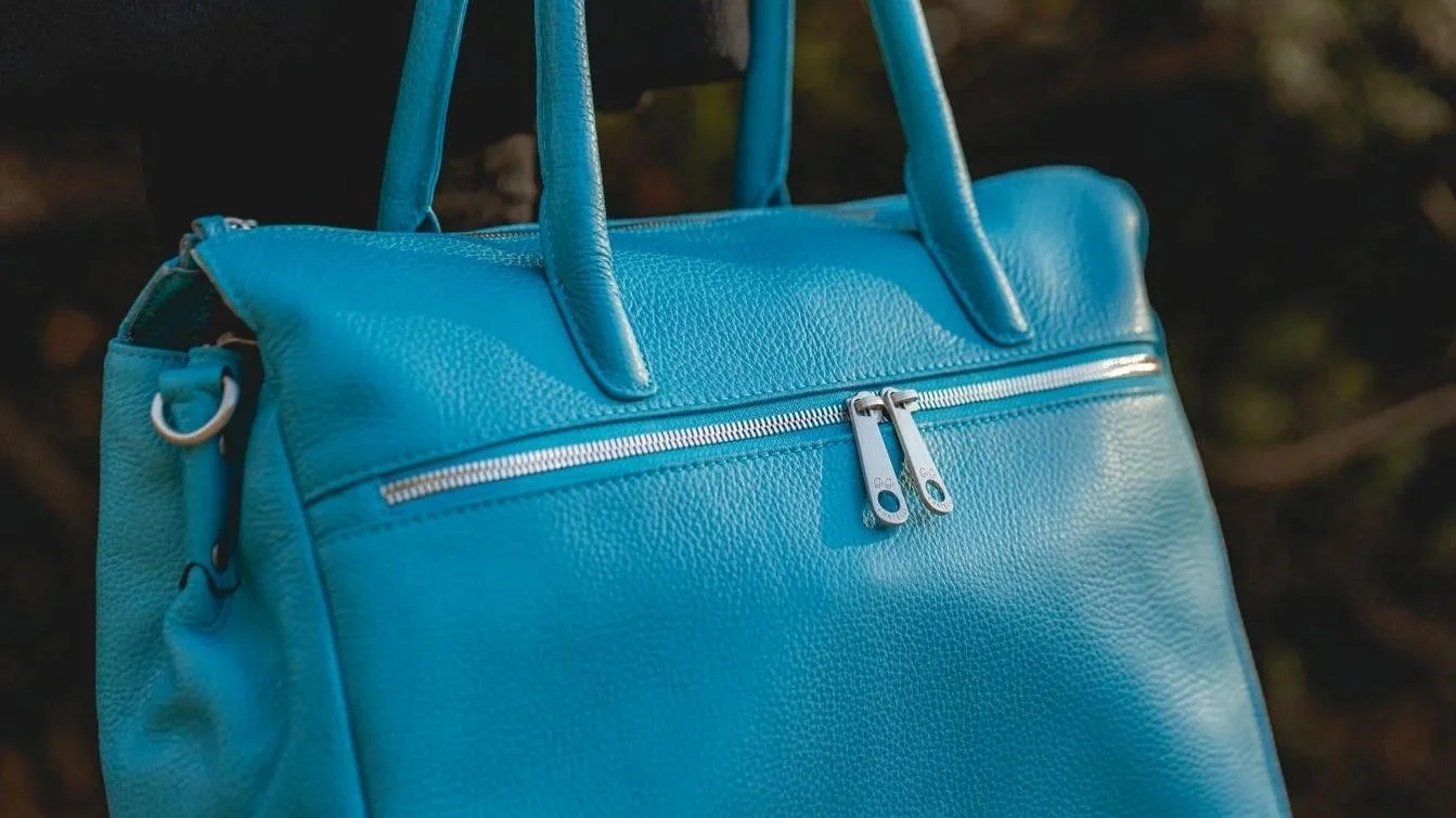 Een blauwe leren tas met ritsen en handgrepen.