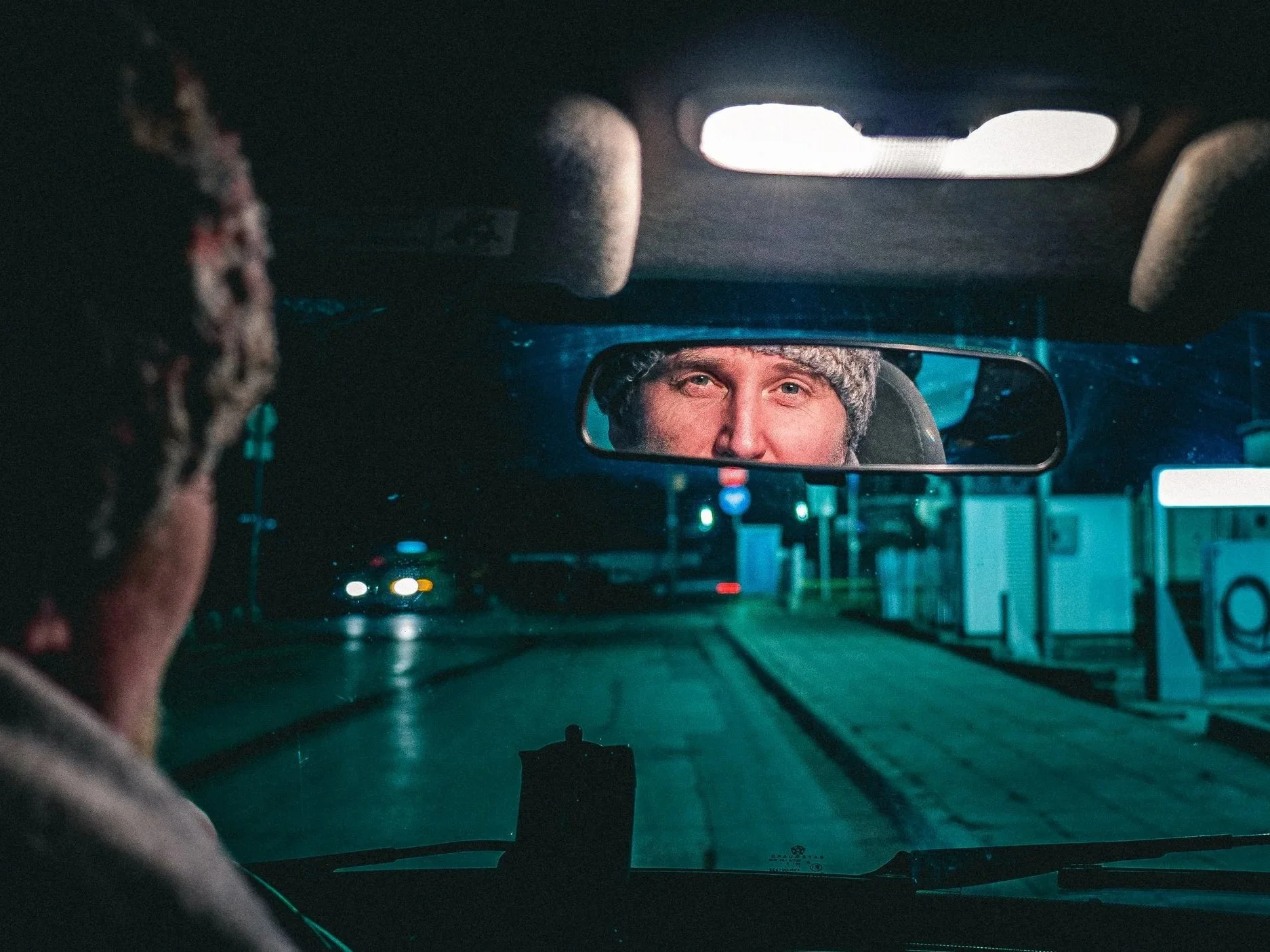 Gezicht van een man dat wordt weerspiegeld in de achteruitkijkspiegel van een auto tijdens de nacht - Storytelling en fotografie door Eleven Monkeys