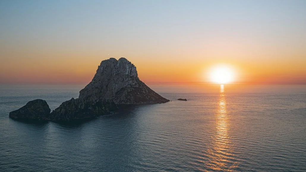 Een zonsondergang boven de oceaan met een grote rotsformatie in het water.