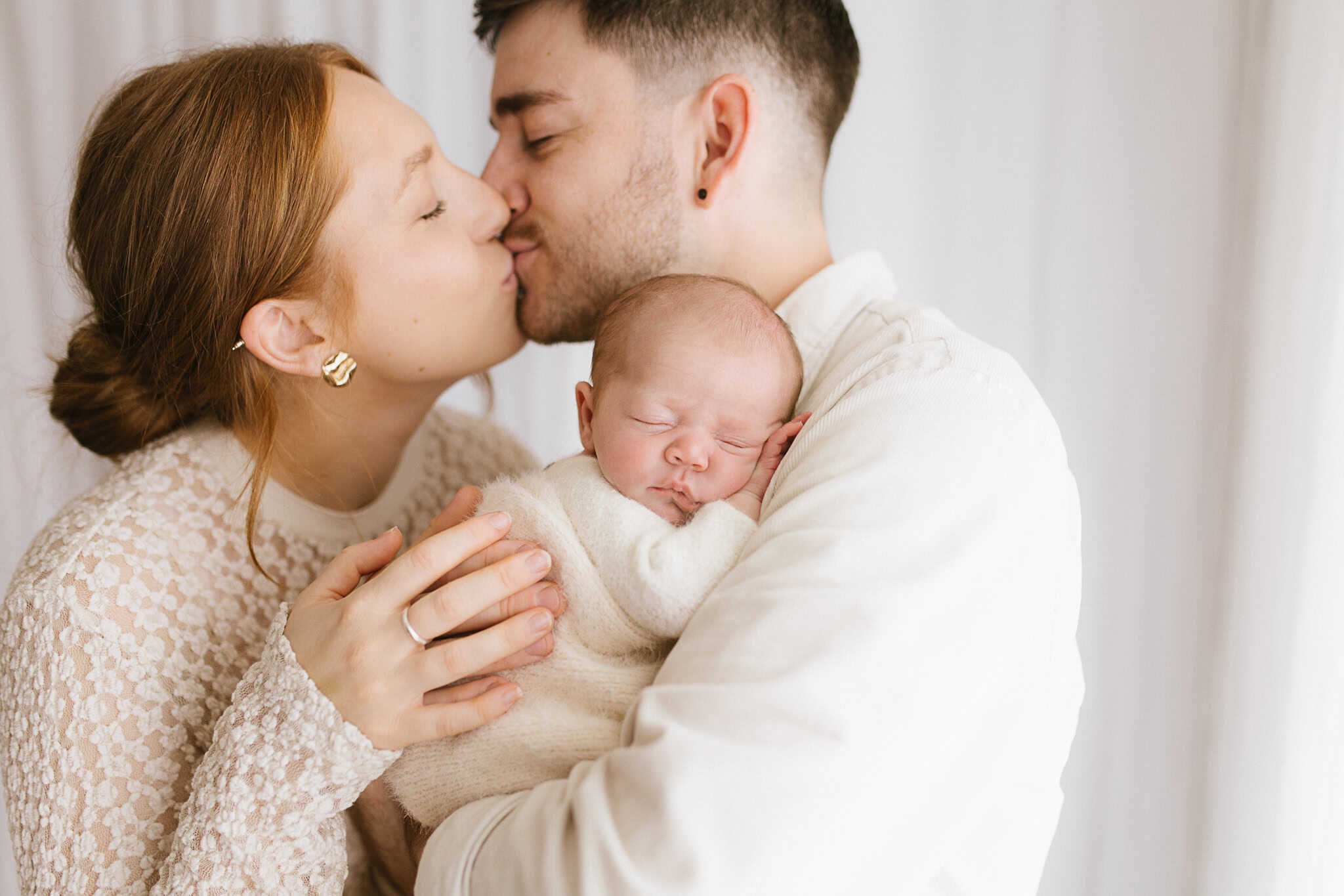 A light and sweet moment as parents share a kiss during newborn photography session in Cornwall