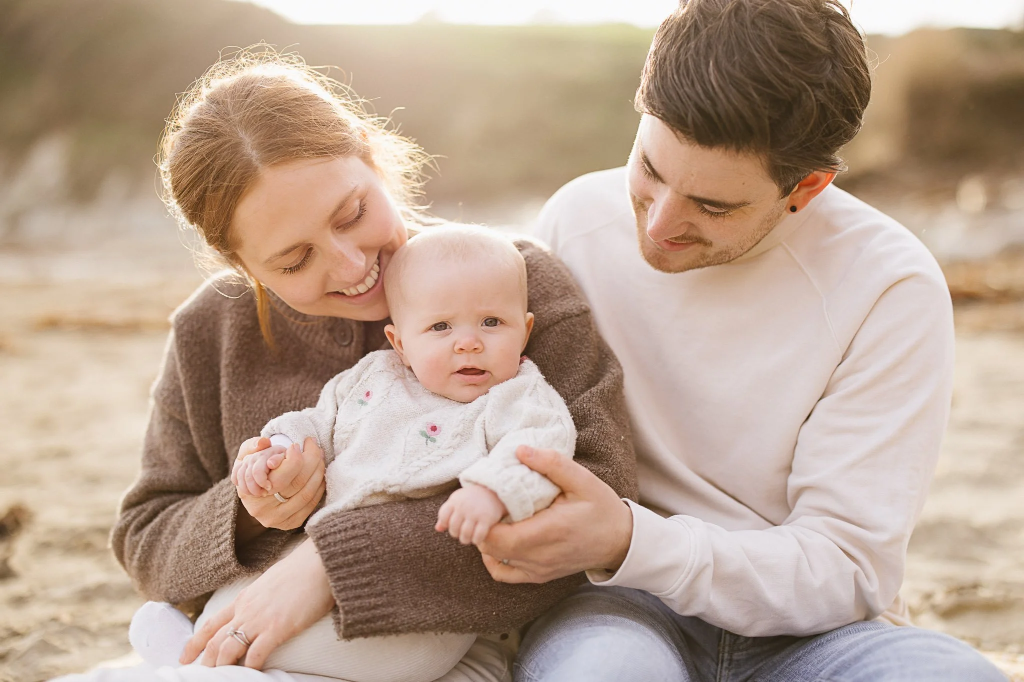 Family with baby share a smile at relaxed beach family photography session in Cornwall