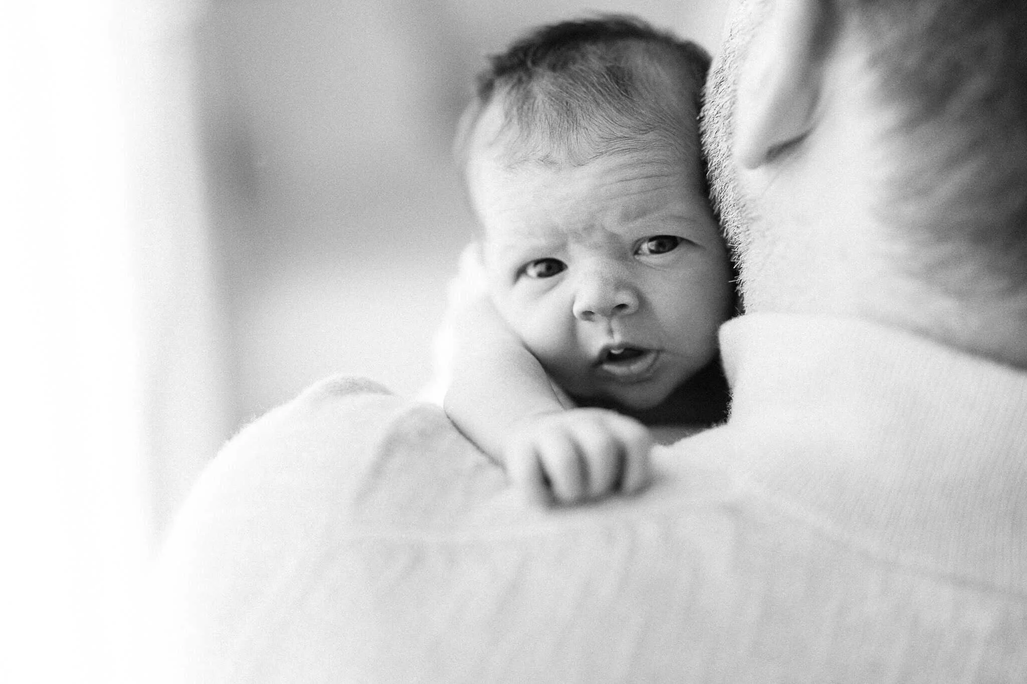 Newborn baby peers over father's shoulder in candid moment during newborn photography session in Cornwall