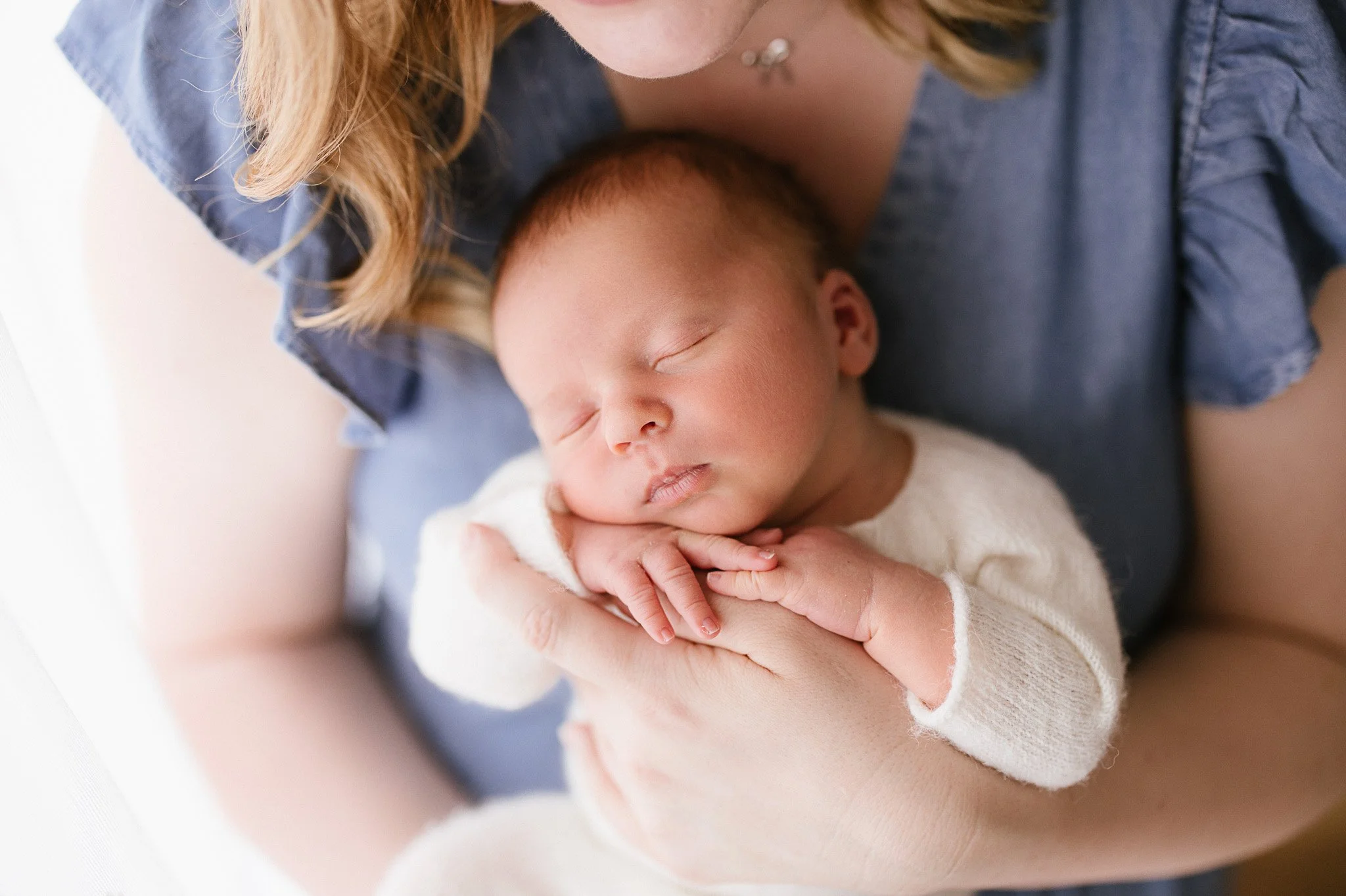 Mother wearing a blue denim dress holding newborn baby during newborn photoshoot in Cornwall