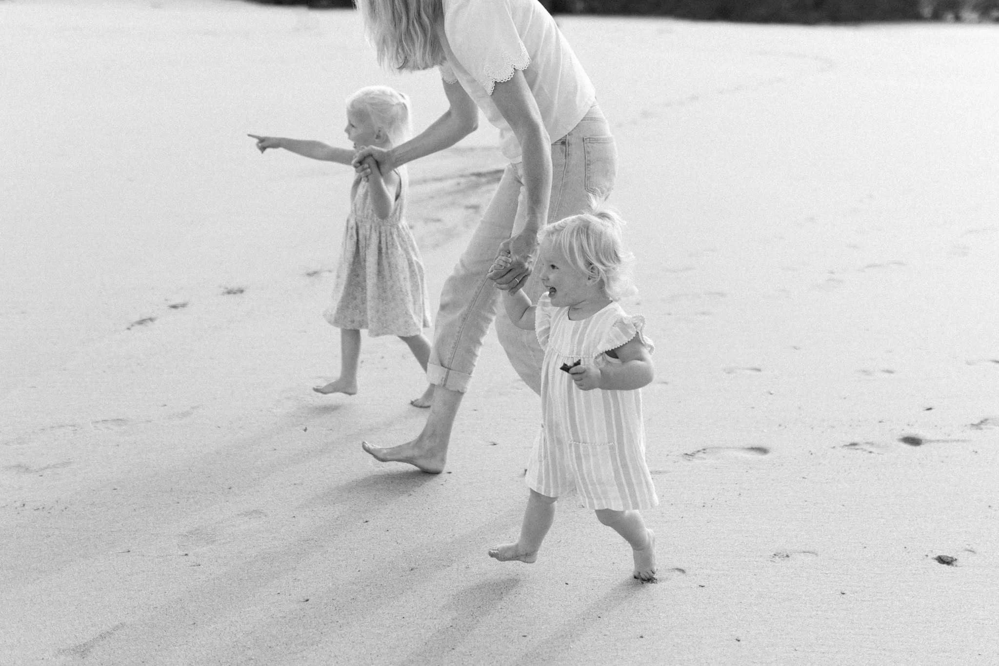 Two small children excitedly walking to the sea with mum during a beach family photography session in Cornwall