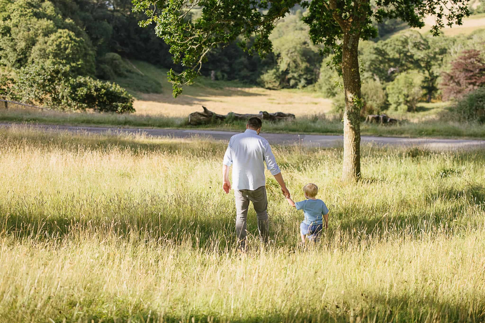 Father and son walking in grass during relaxed family photoshoot at Trelissick in Truro, Cornwall