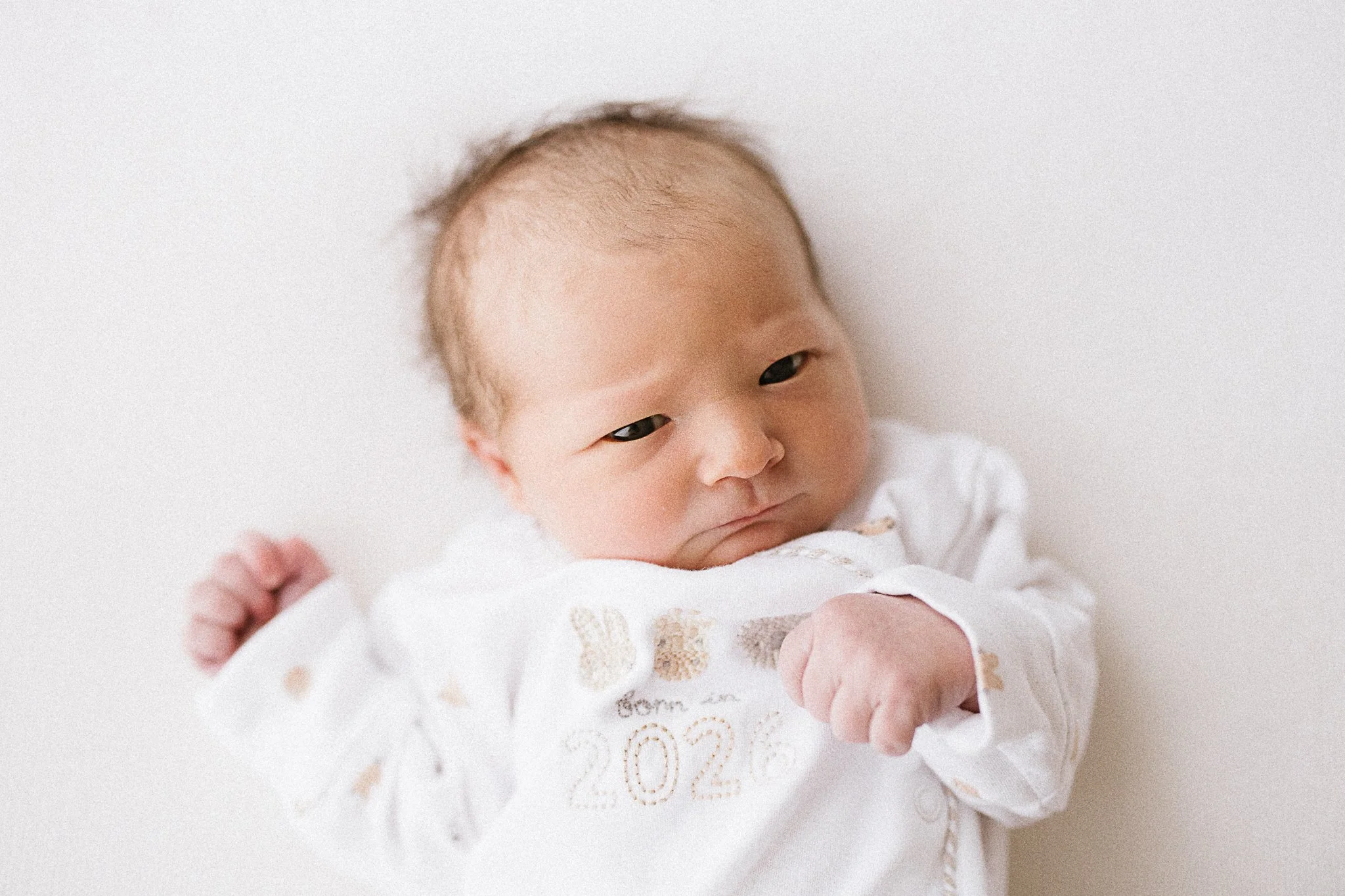 Newborn baby with wide eyes in a white outfit, natural newborn photography in Cornwall