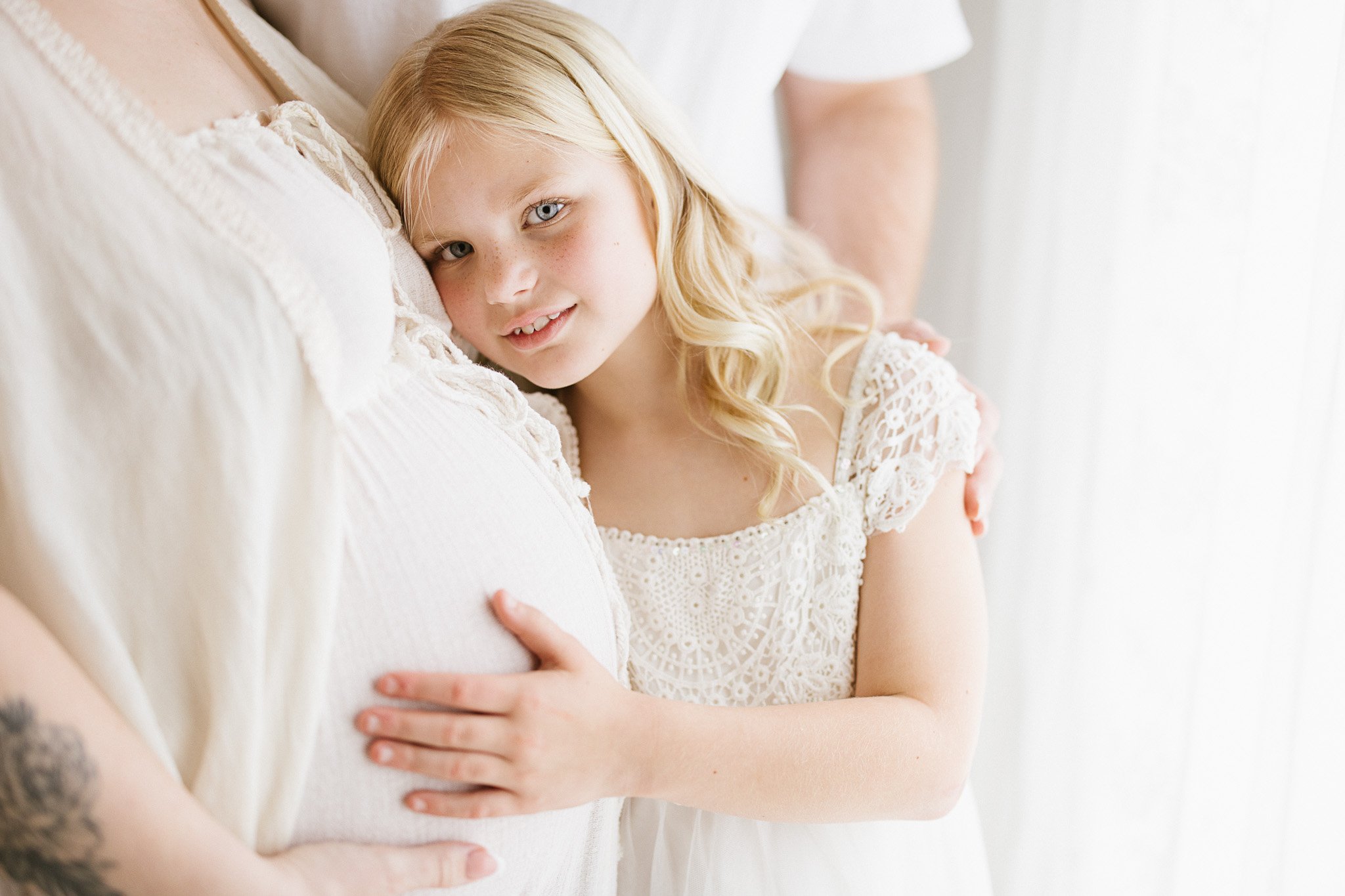 Girl hugs pregnant mums bump in a soft moment during a natural light maternity photography session in Cornwall