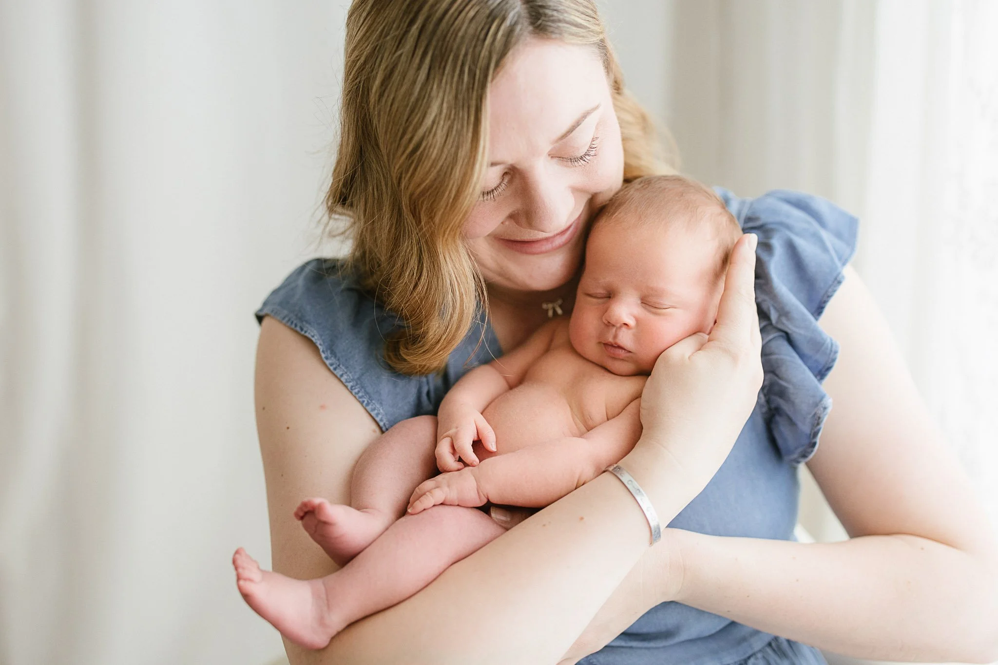 Mother wearing denim blue dress and baby photo during newborn photoshoot in Cornwall