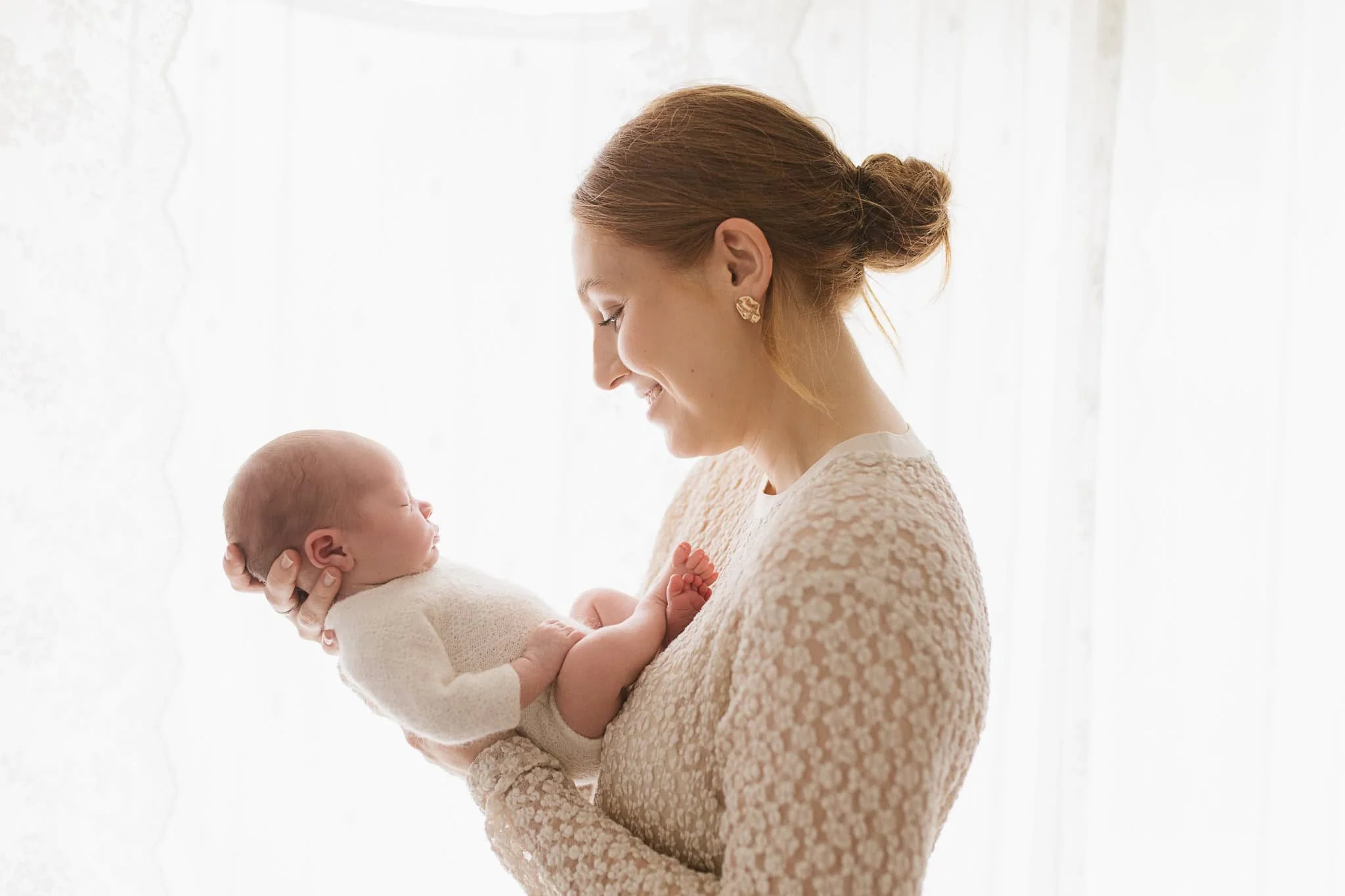 Mother wearing lace dress with newborn wearing knitted romper during newborn photography session in Cornwall