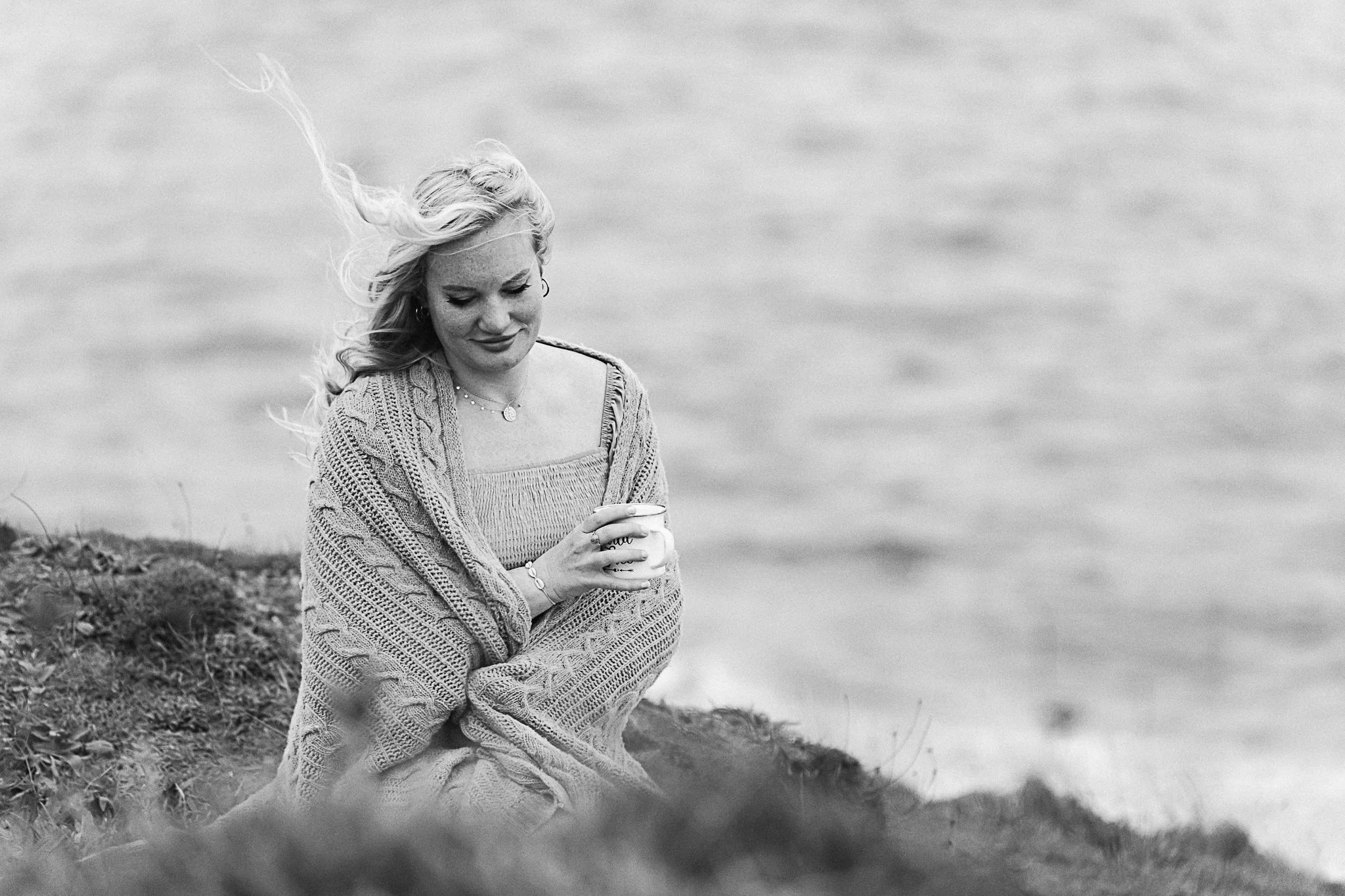 A soft introspective photo of women sitting on Cornish coast cliff during her sunrise portrait photography session