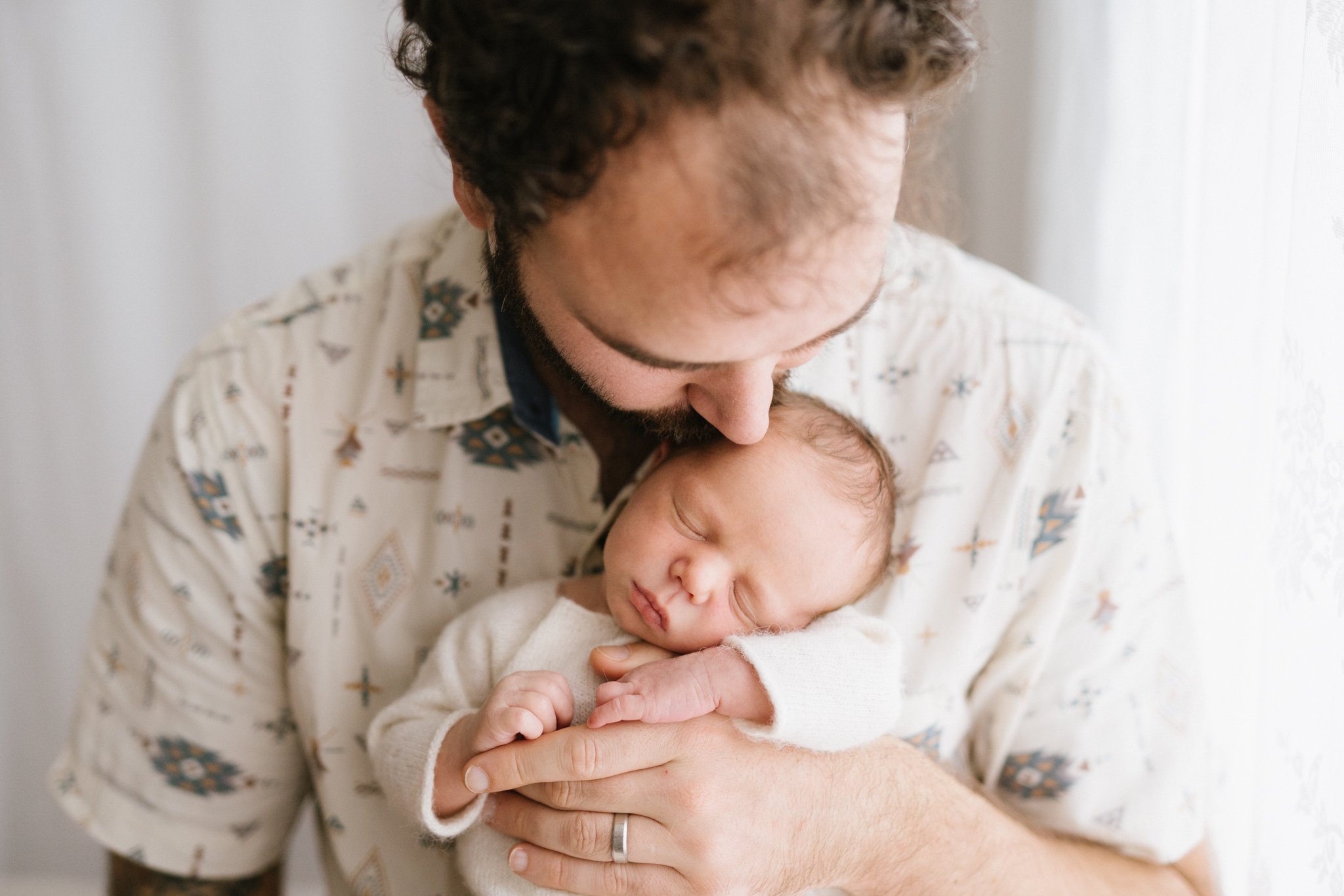 Father wearing patterned shirt with newborn baby boy during newborn photography session in Cornwall