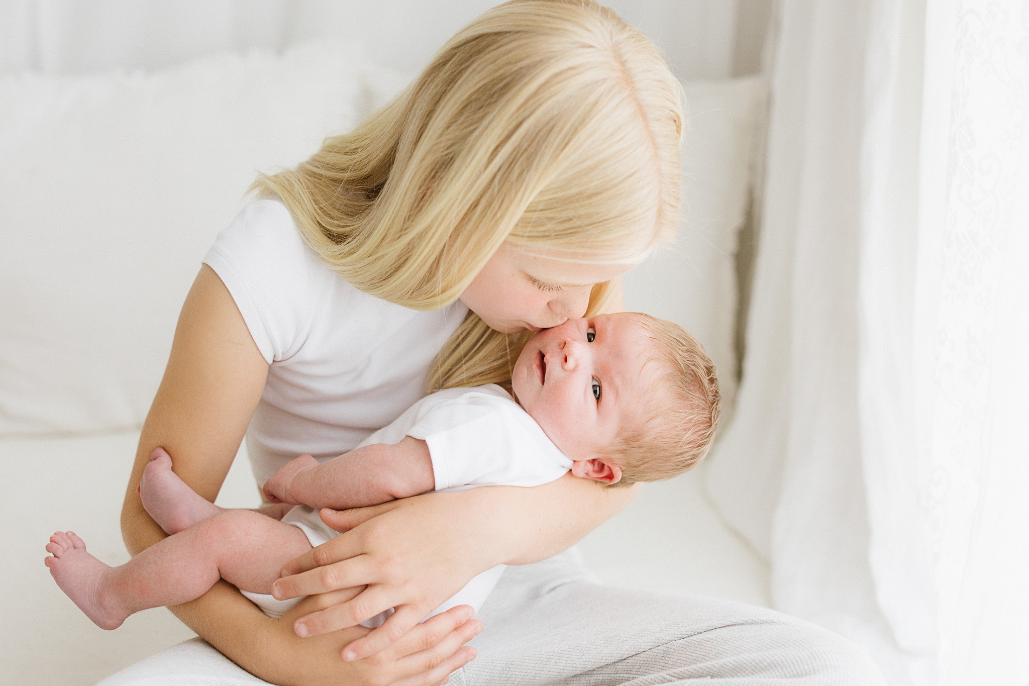 9 year old girl kissing baby sister during natural newborn photography session in Cornwall
