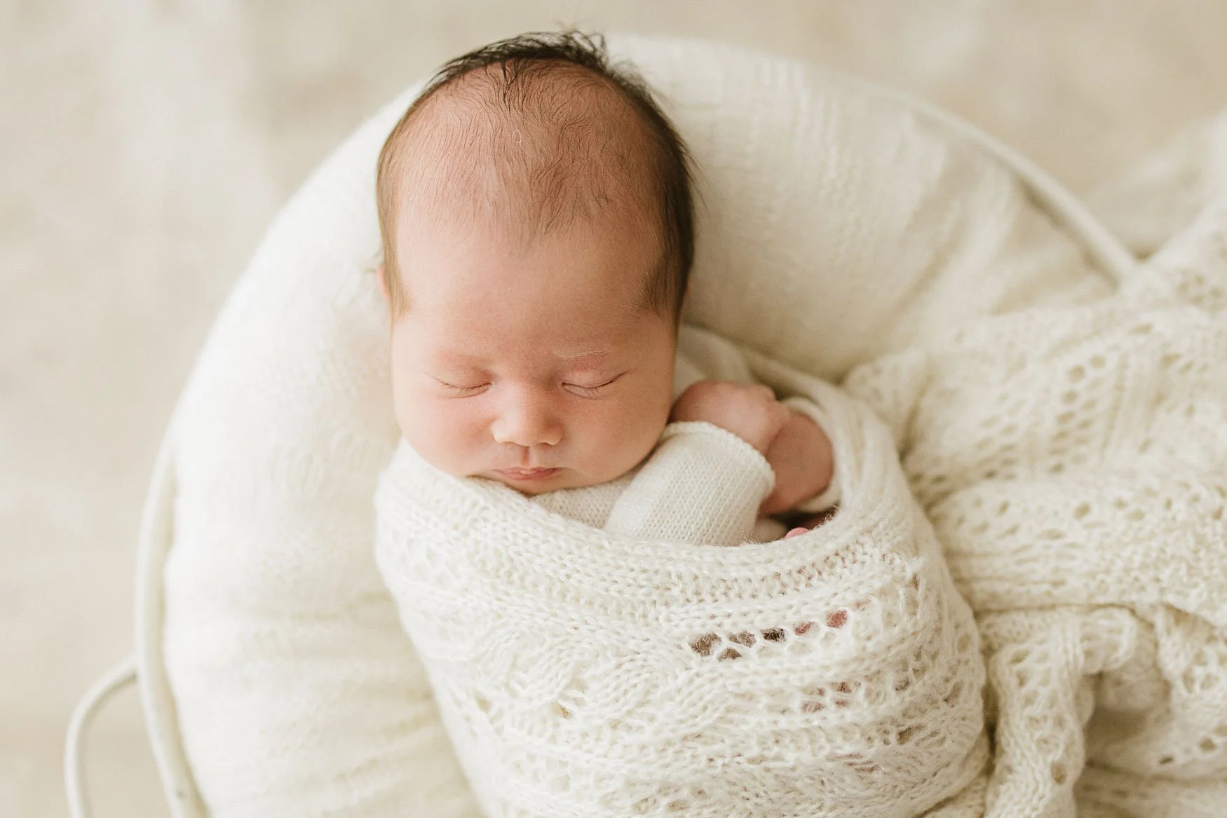 A peacefully sleeping newborn baby wrapped in organic cream linen during a Cornwall photography session