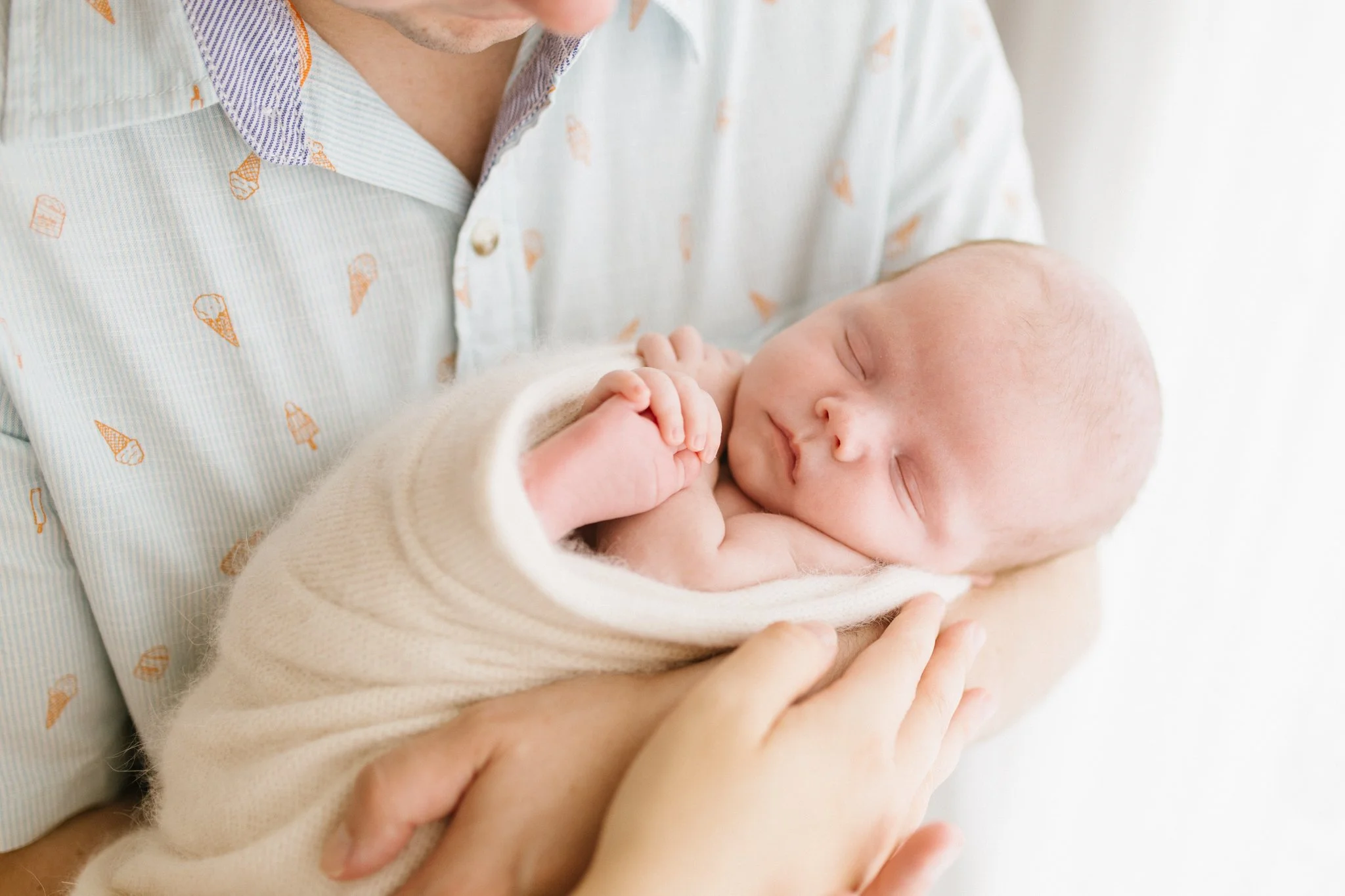 Father wearing a light blue shirt holding newborn baby girl during newborn photography session in Cornwall