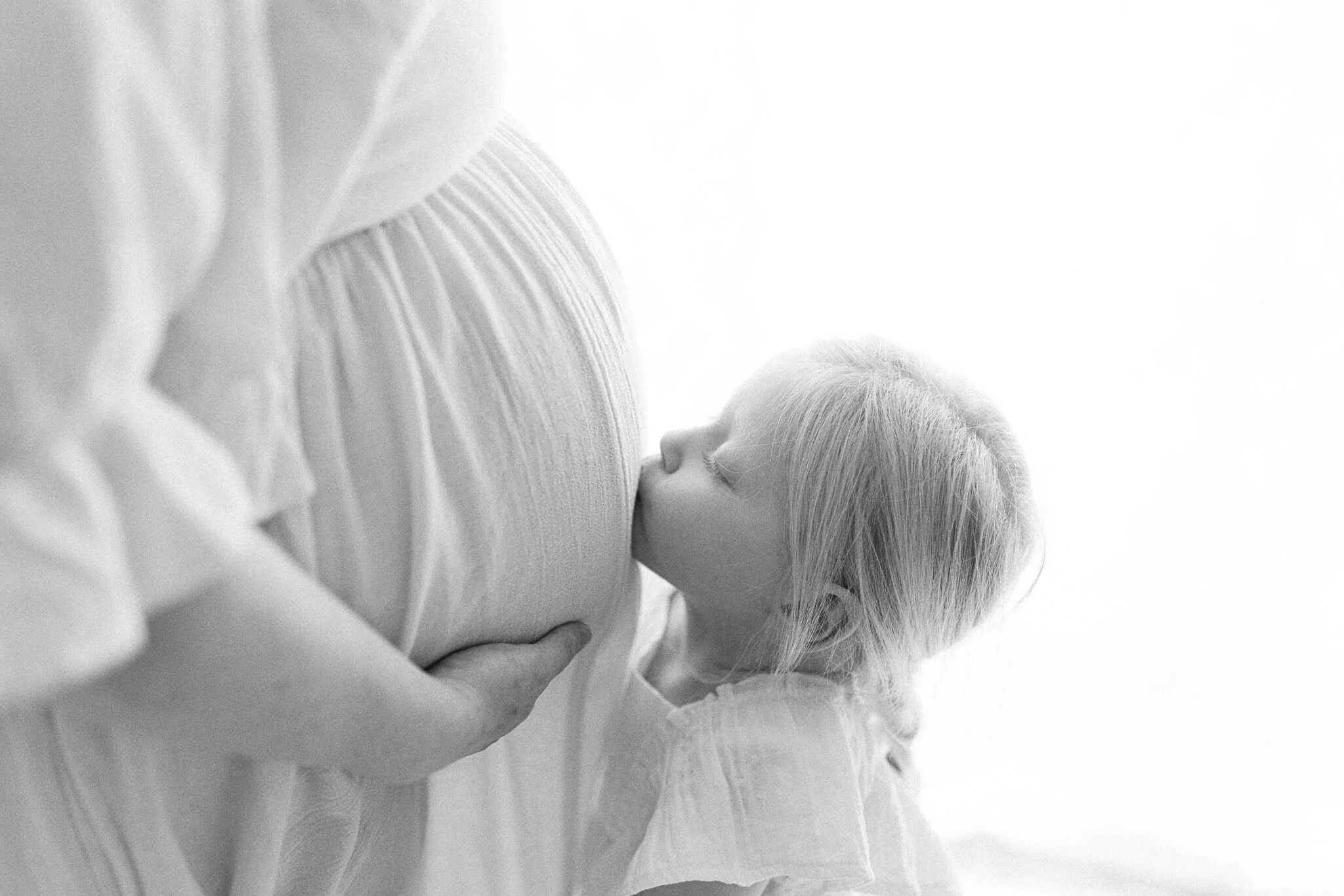 Child kisses mums pregnant belly during natural maternity photoshoot in cornwall studio