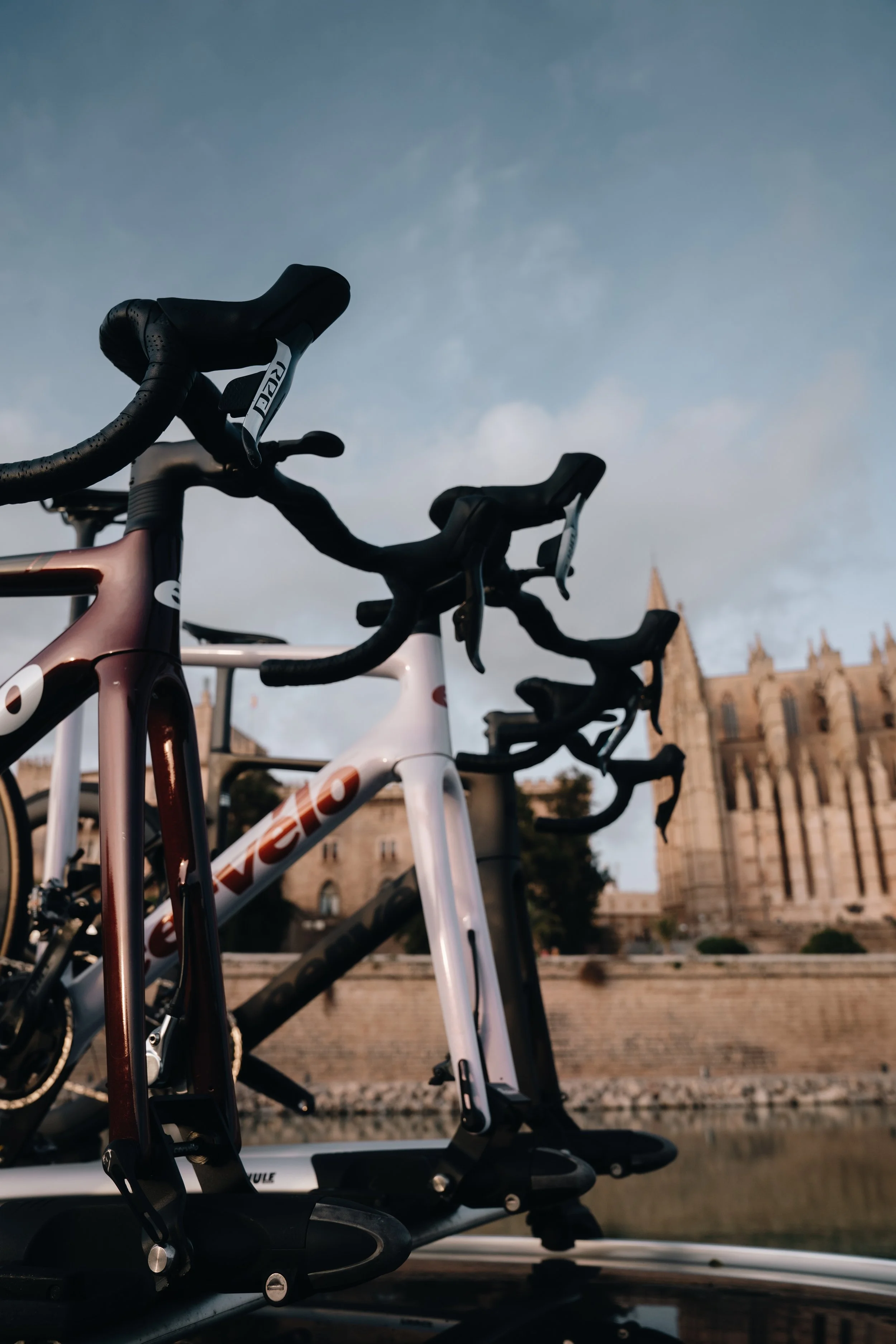 Two bicycles parked outdoors with a historic cathedral in the background, under a cloudy sky.