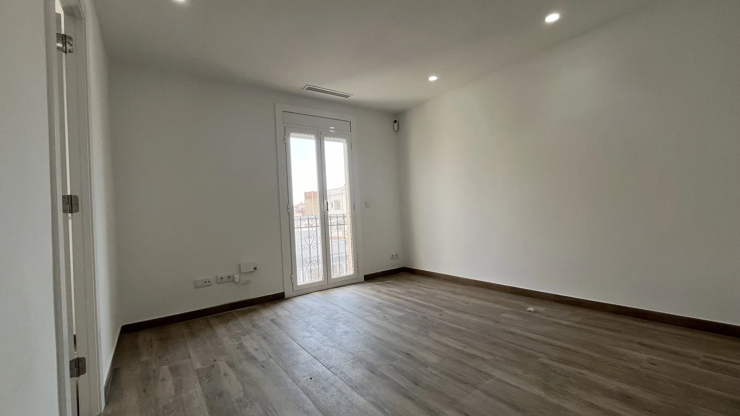 Habitación vacía con puerta con balcón de cristal, suelo de madera y paredes blancas.