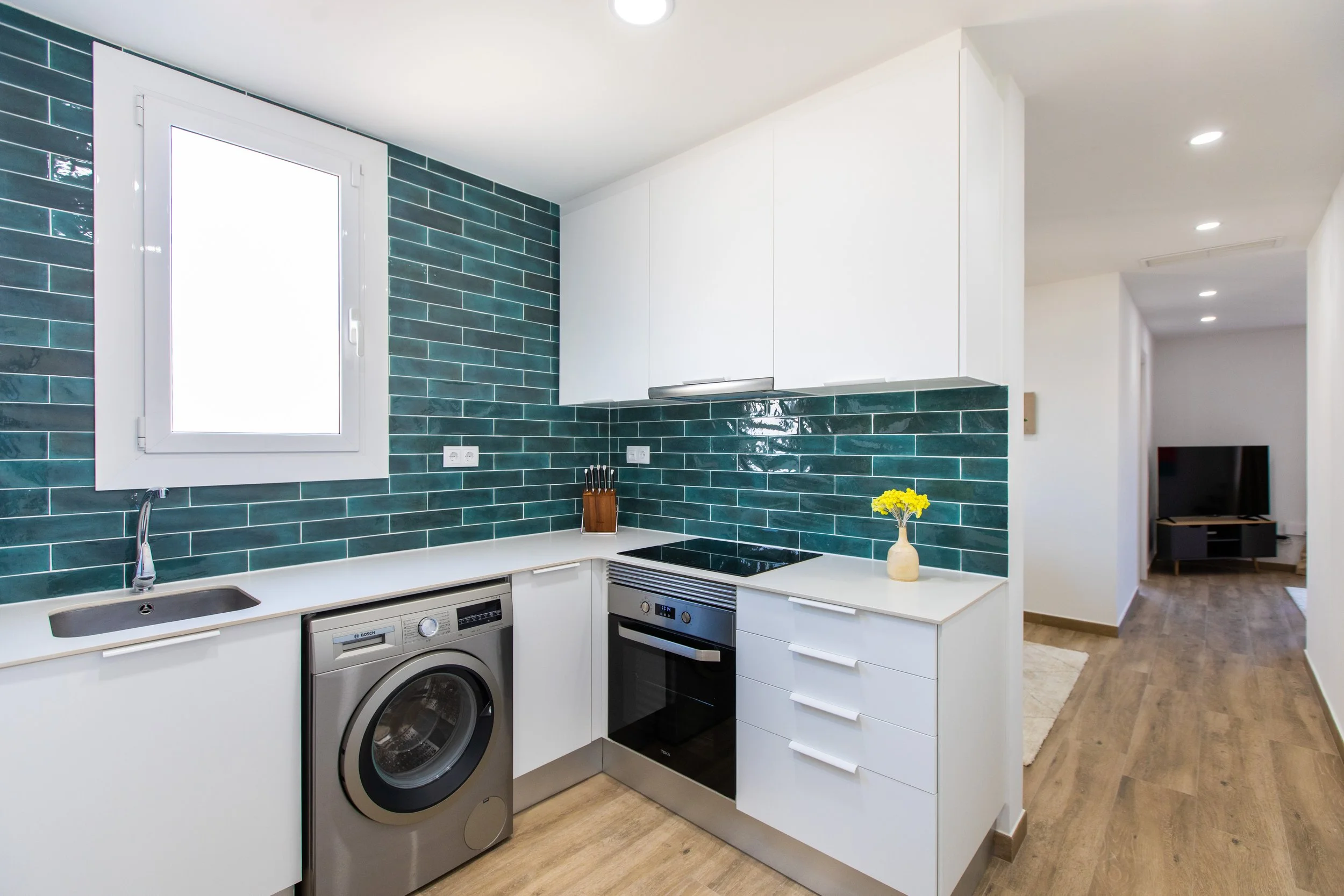 Cocina moderna con azulejos verdes, electrodomésticos de acero y una ventana