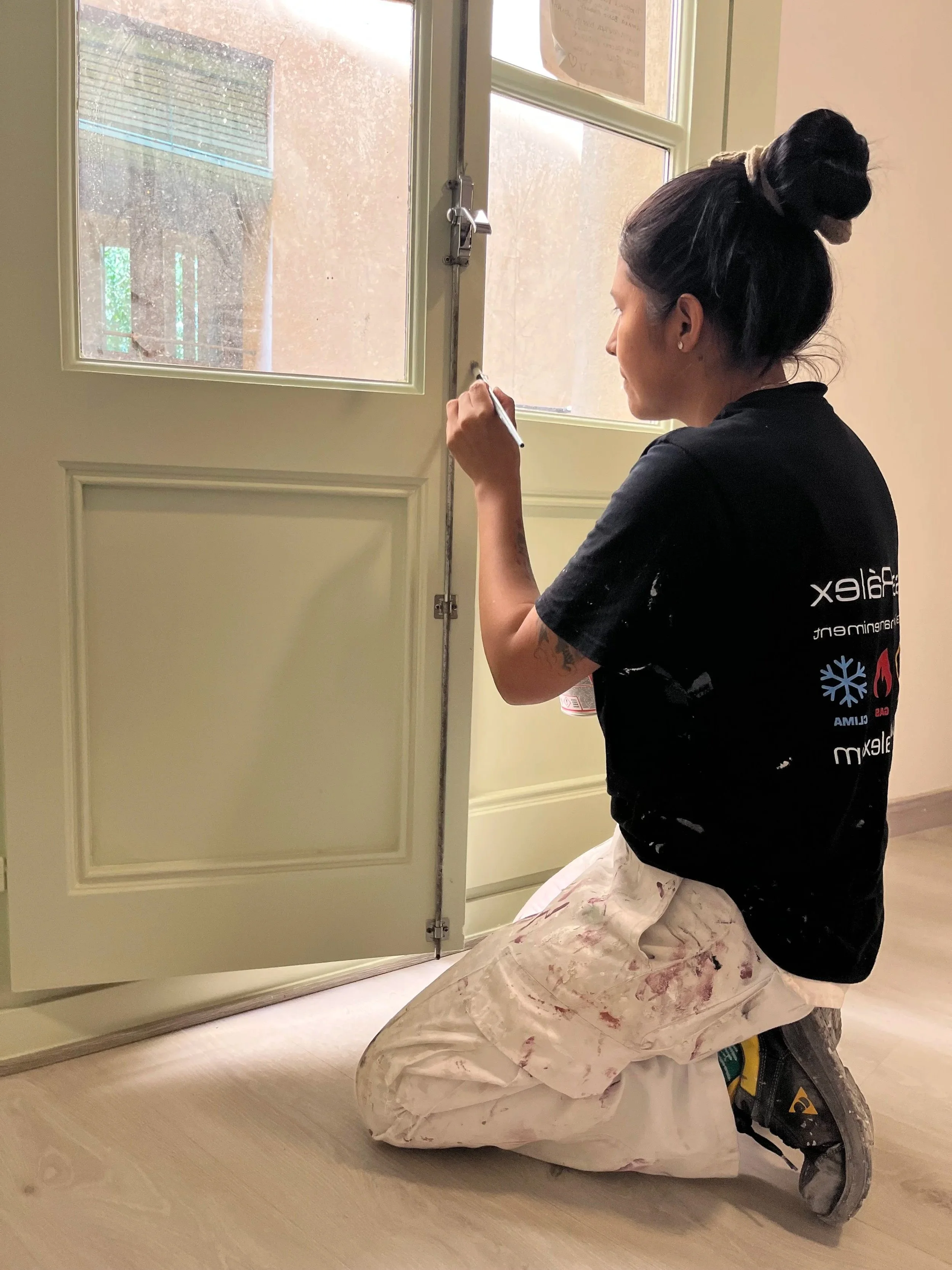 Una mujer trabajando en la instalación de una puerta o ventana de color beige en un interior, ella está en posición en cuclillas, usando pintura o marcador para marcar o medir.