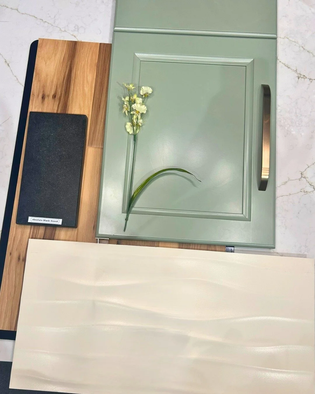 This mood board brings together a refreshing and grounded kitchen palette that feels modern and organic. The soft sage-green cabinetry adds a calming, natural touch, accented by a sleek brushed bronze handle. The natural wood flooring introduces warm