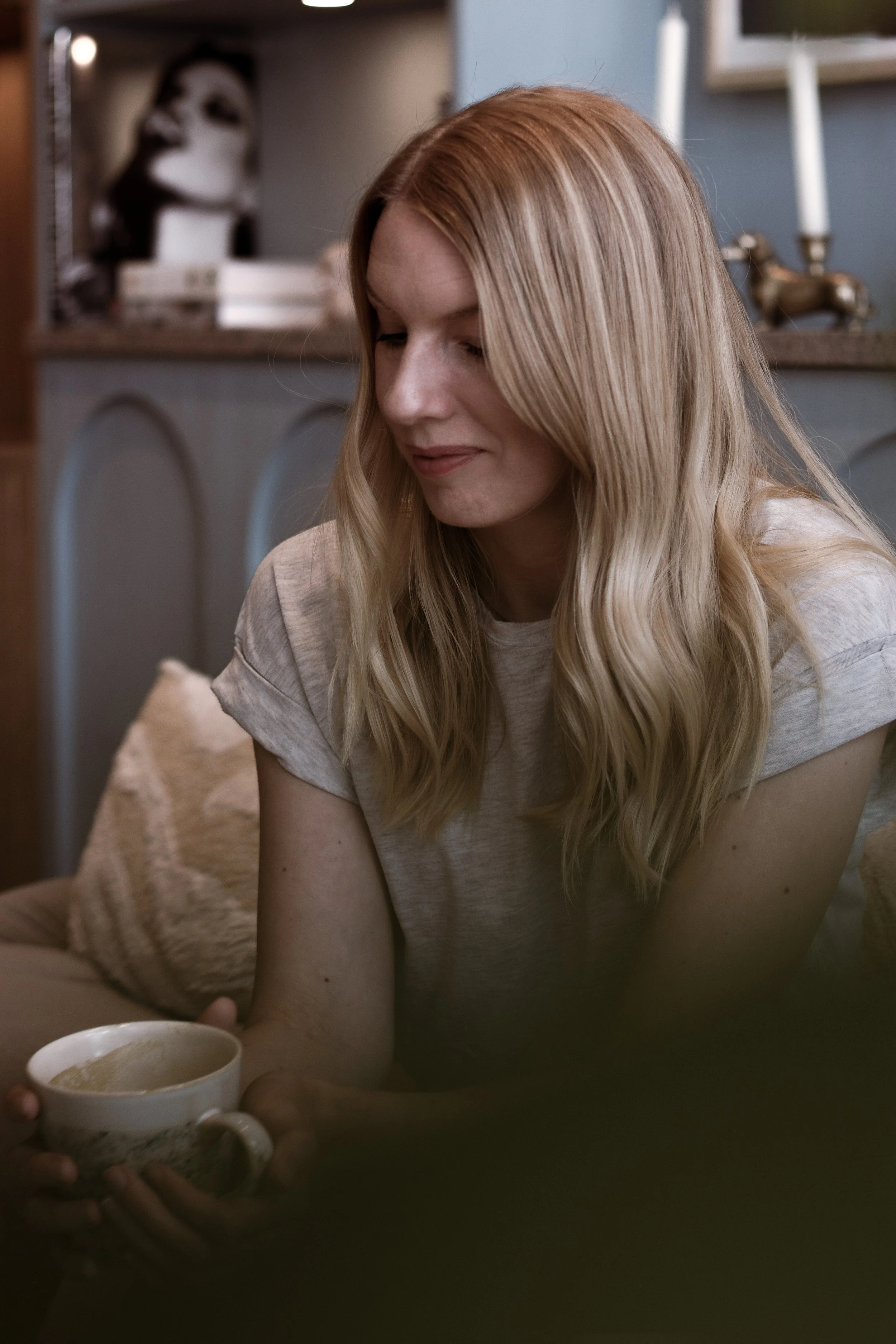 Kvindelig person med blondt hår, der sidder i en stue og modtager en kop te.