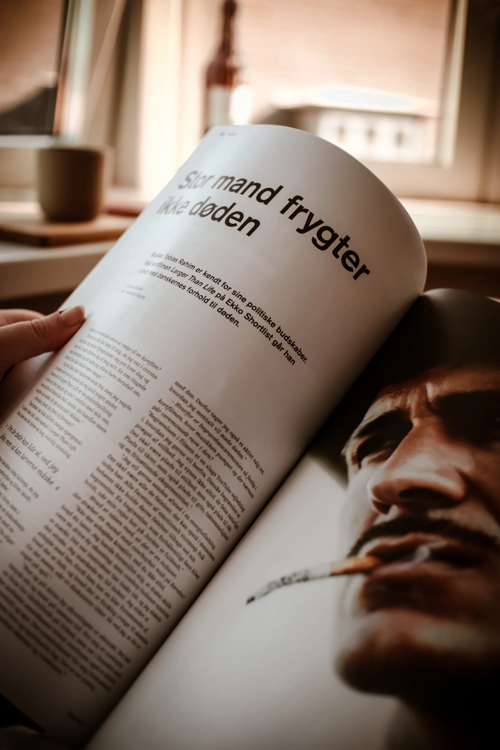 En person læser en avis eller et magasin med en artikel, der har overskriften 'Stor mand frygter ikke døden'.